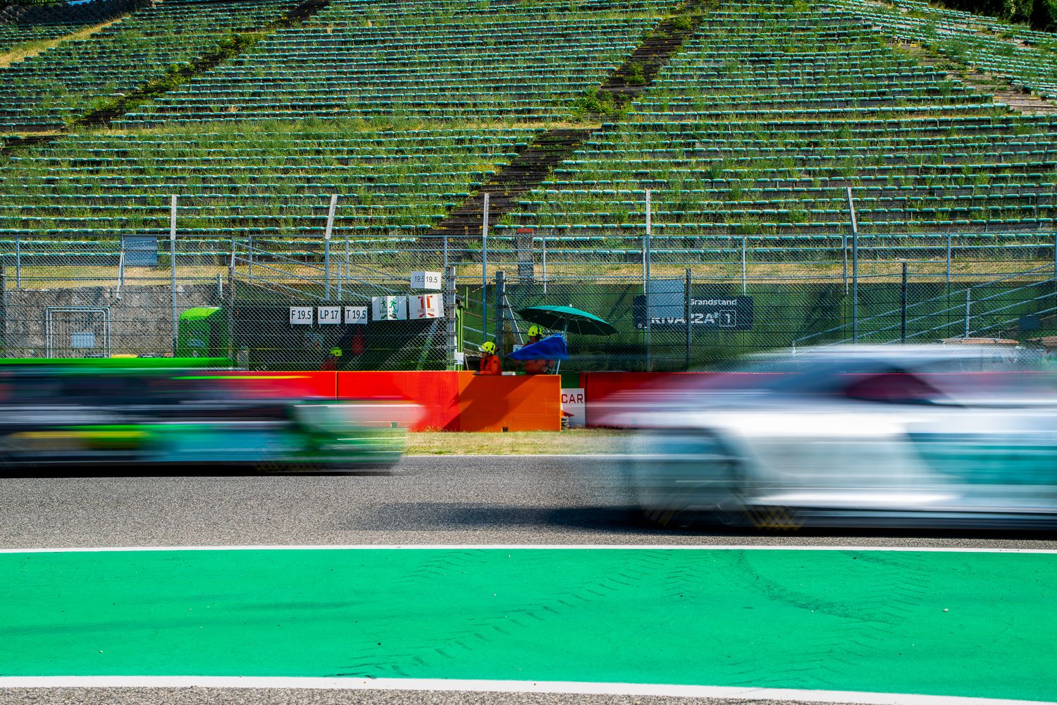 Panning shot with strong motion blur of racing cars speeding past the main grandstand of a racetrack.