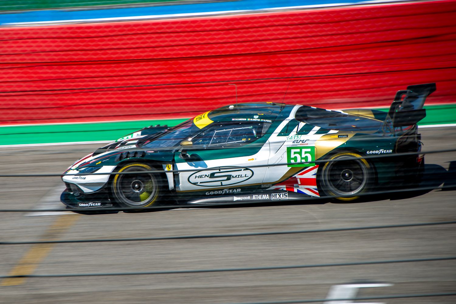 Green and white racing car number 55 speeding on the asphalt track with a red and white barrier background.