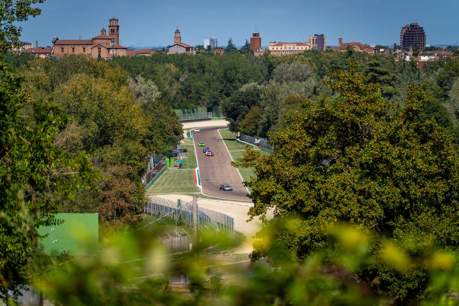 A panoramic view of Imola’s racetrack surrounded by trees, with the city skyline visible in the distance.