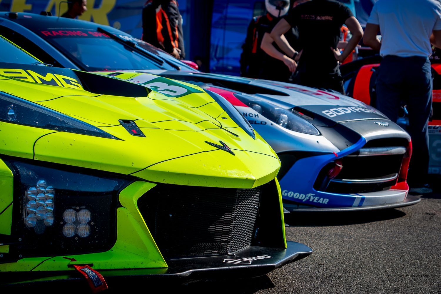 Front view of vibrant lime green and blue motorsport racing cars lined up in the paddock before the race.