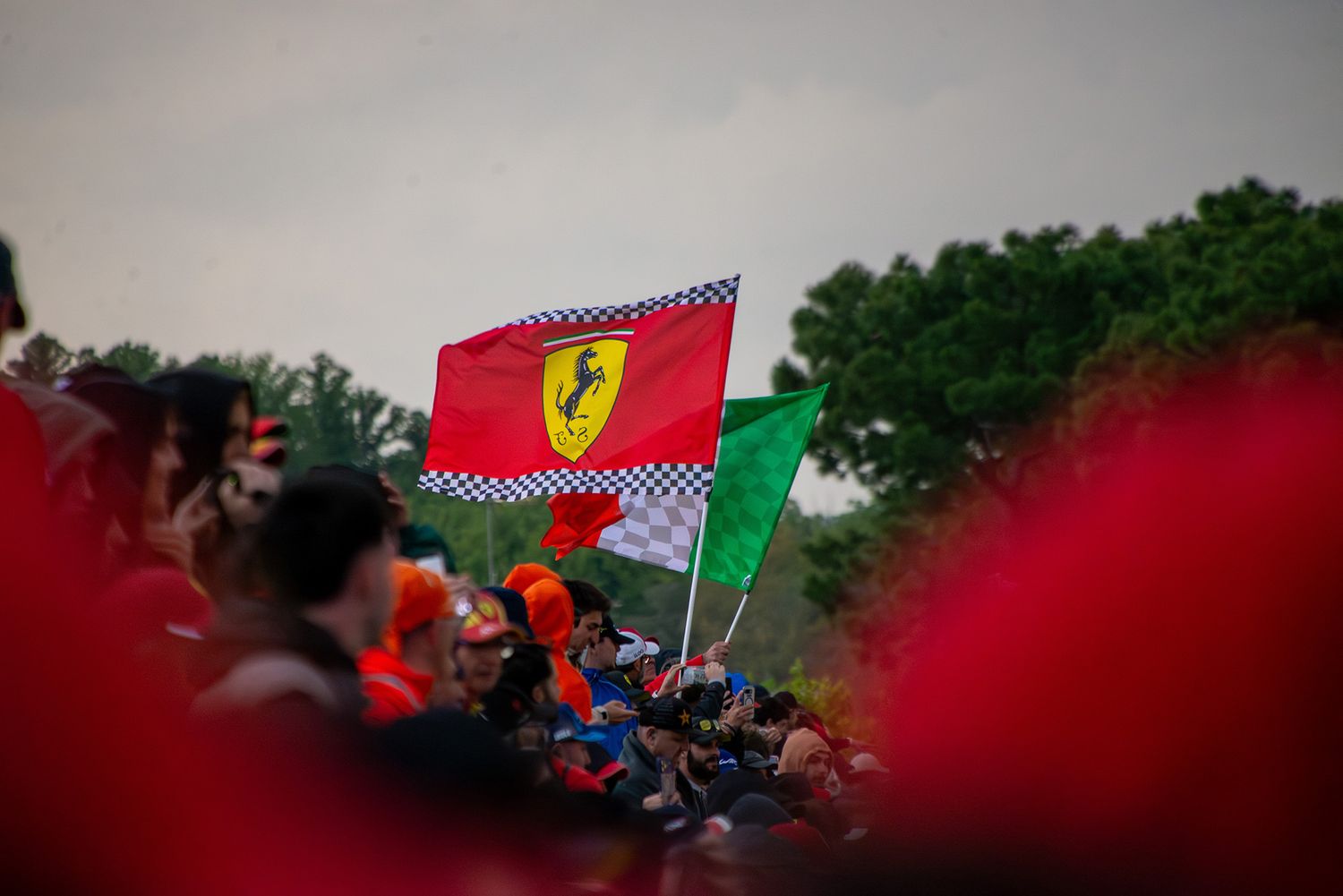 A large red Ferrari flag waving proudly above a blurred crowd of spectators at the racetrack.