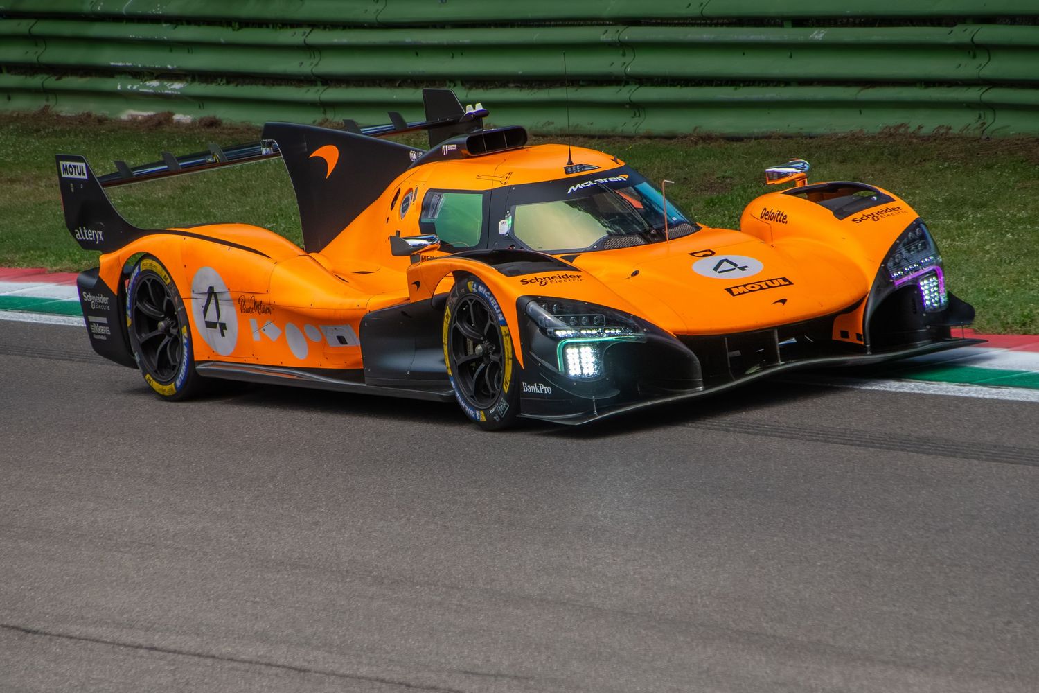 Front three-quarter action shot of the orange McLaren Hypercar rounding a corner on a racetrack.
