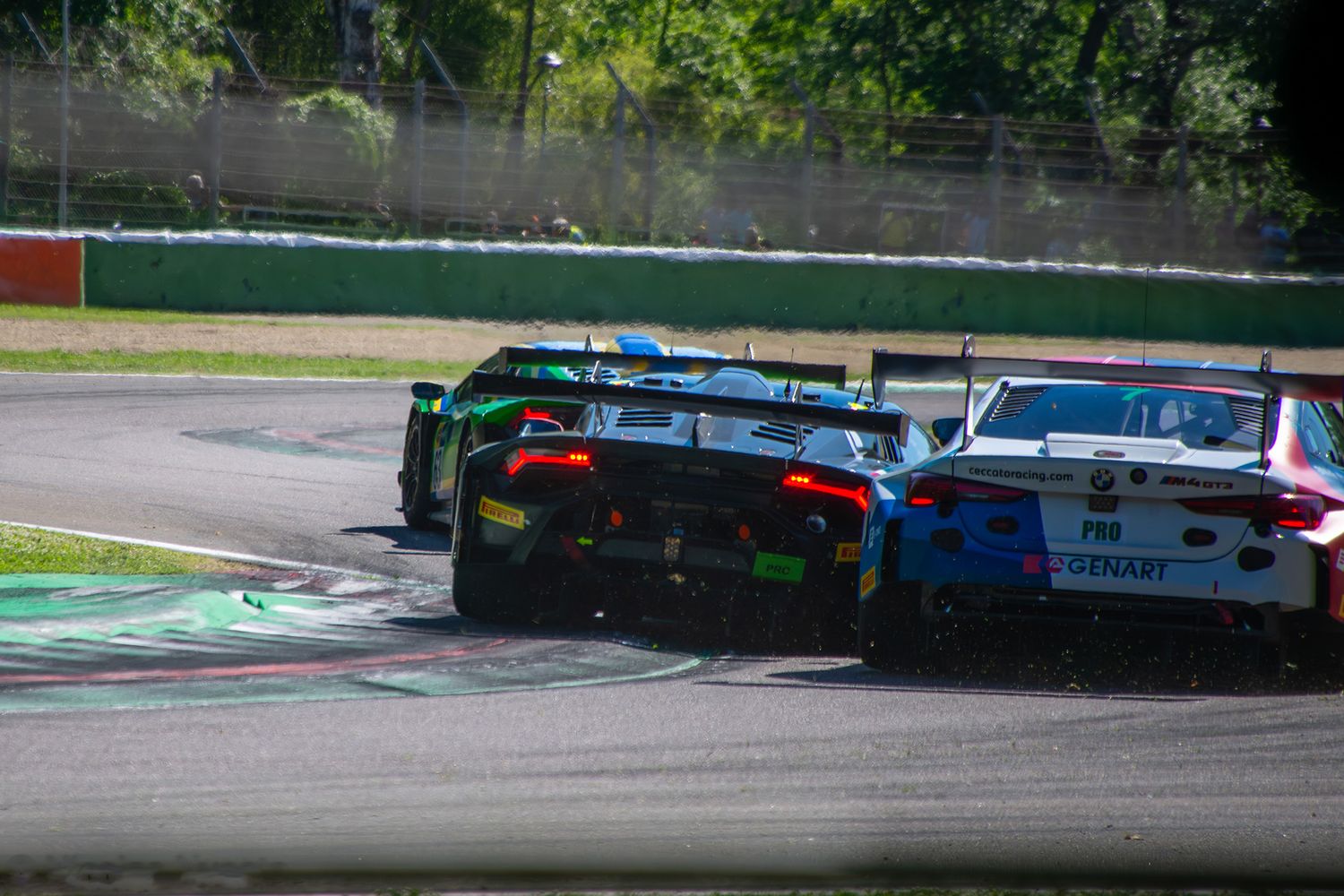 Rear view of multiple GT3 race cars battling closely over a curb during the ACI Racing Weekend.