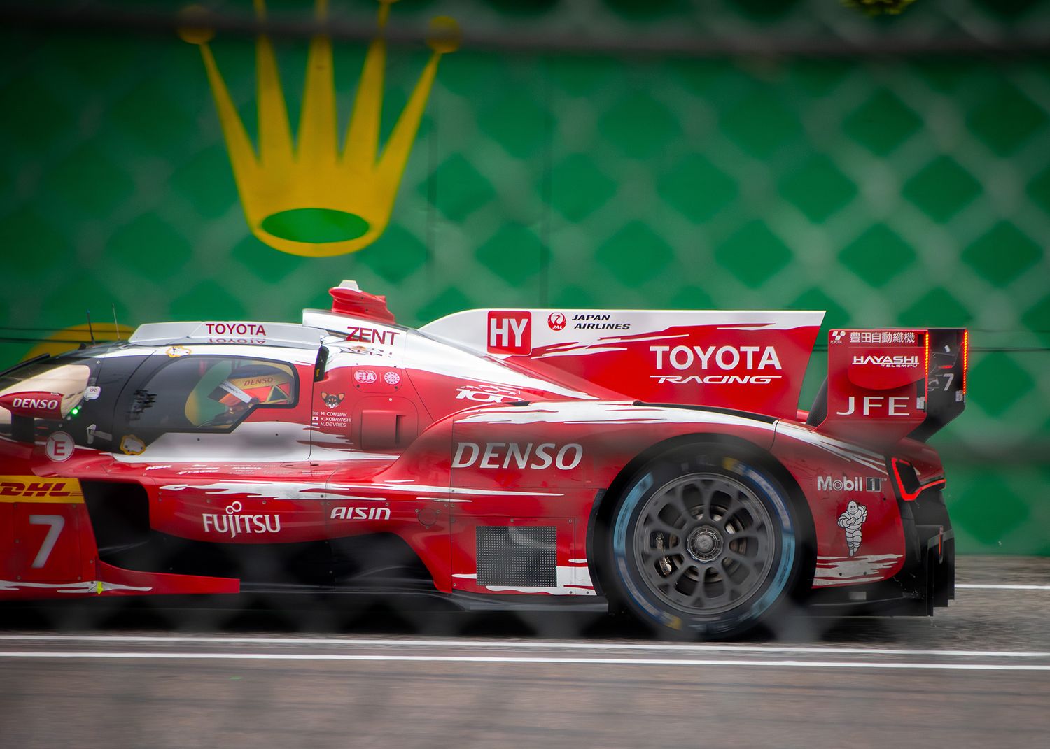Red and white Toyota Hypercar racing behind a catch fence under the iconic Rolex crown logo.