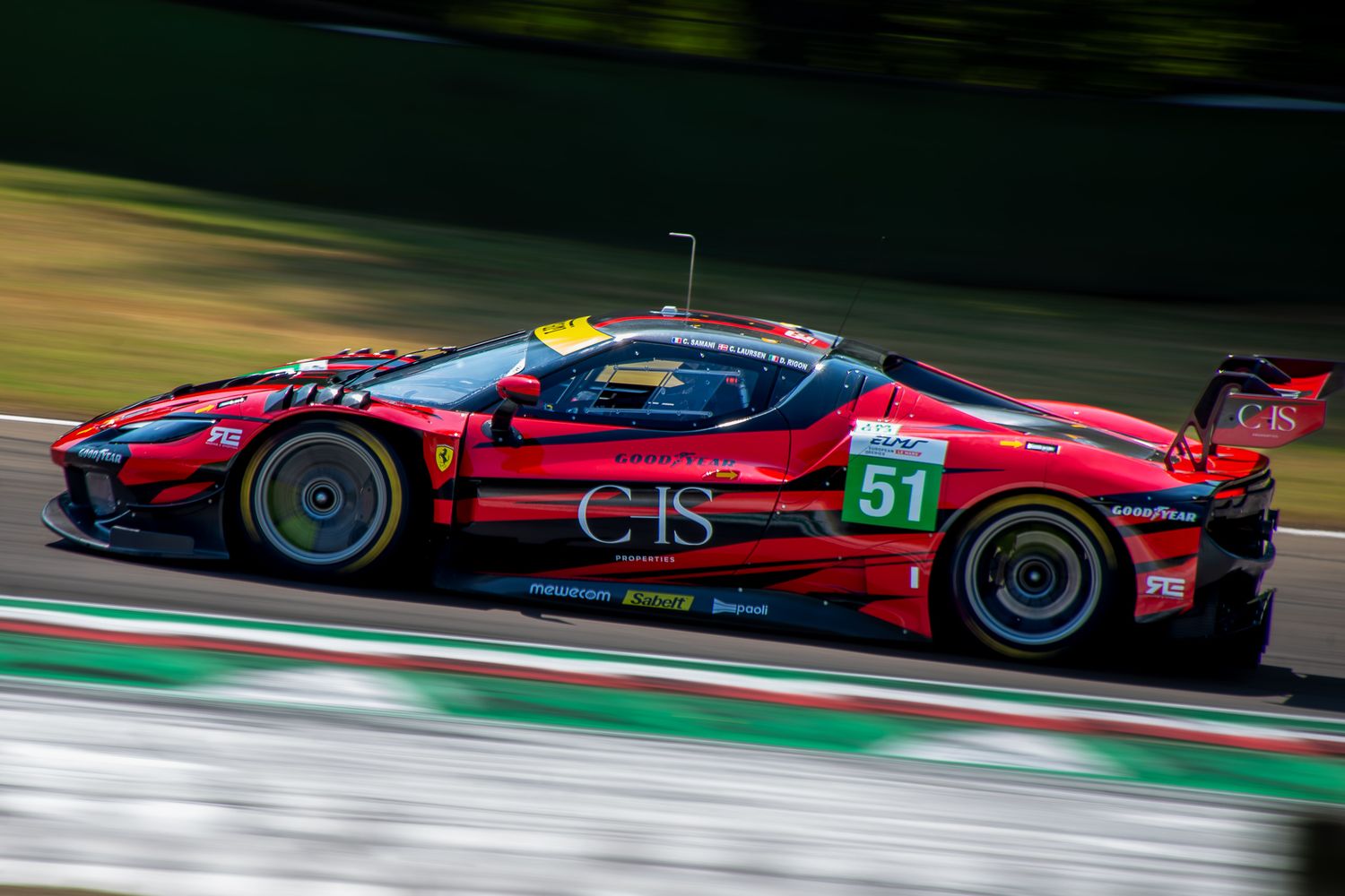 Side view of the red Ferrari number 51 racing car speeding on a track with motion blur effect.