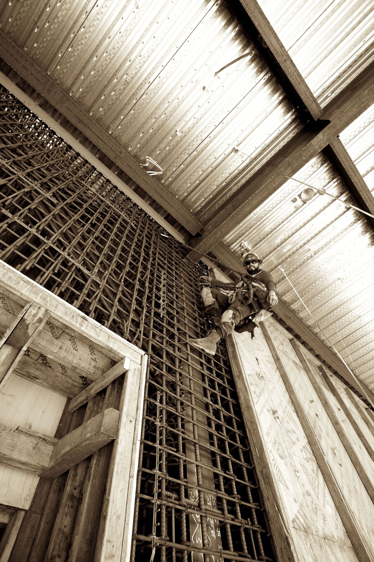 Worker climbing a rope ladder inside a wooden construction framework with metal roofing overhead.