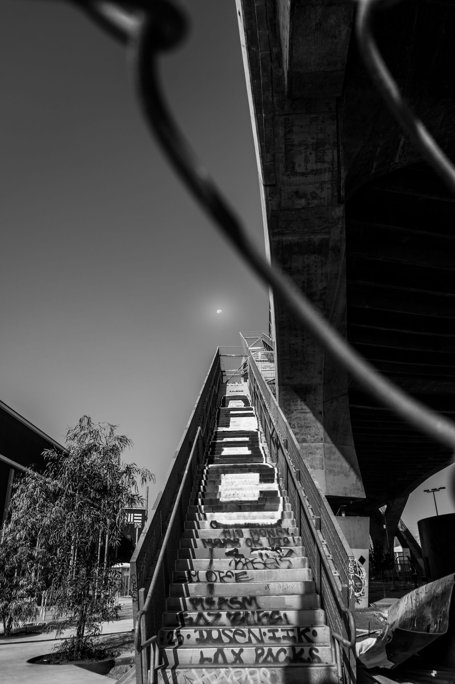Black and white photo of graffiti-covered stairs beneath a concrete overpass with a full moon visible in the night sky.