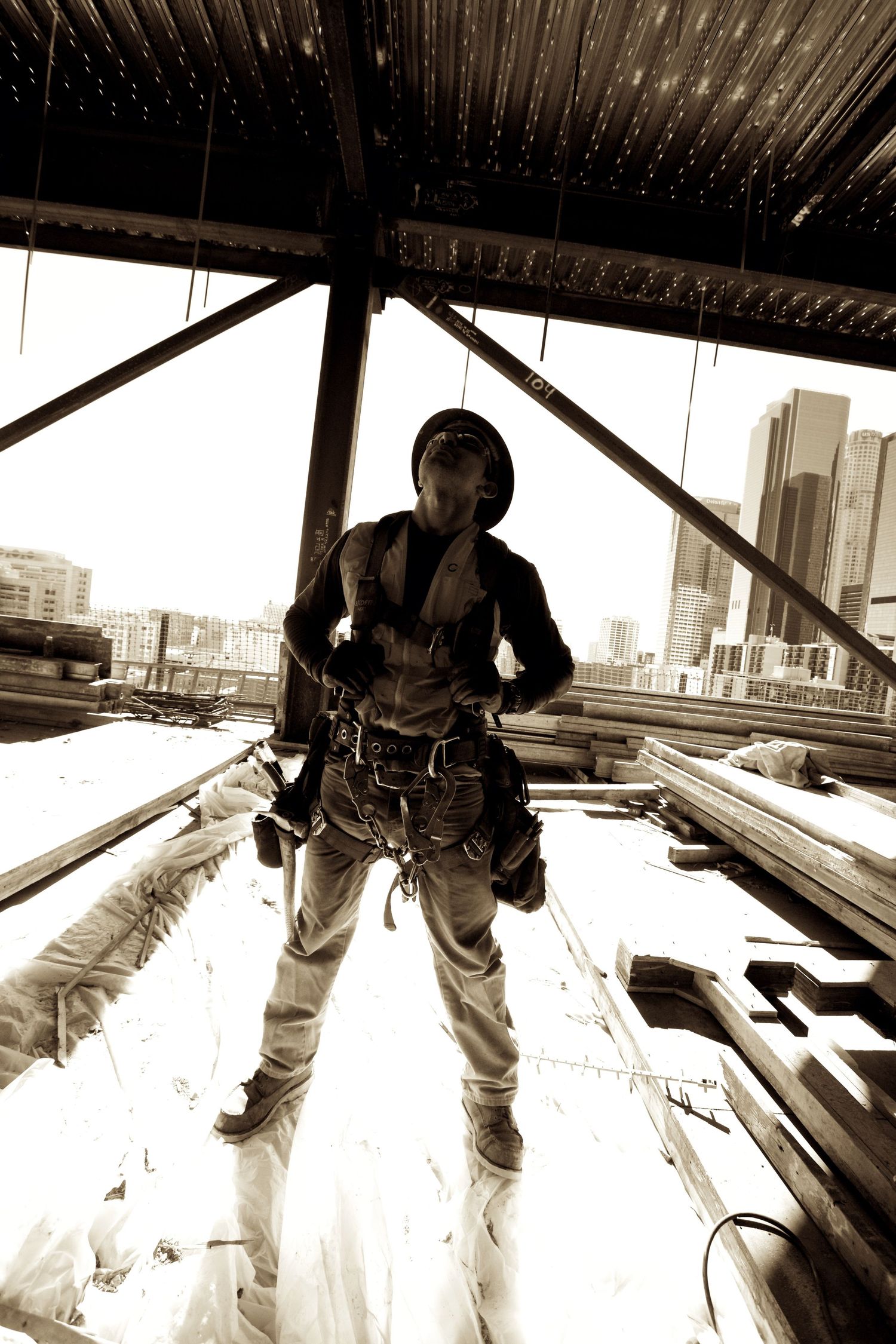 Sepia toned photo of a construction worker in safety harness standing on a steel beam.