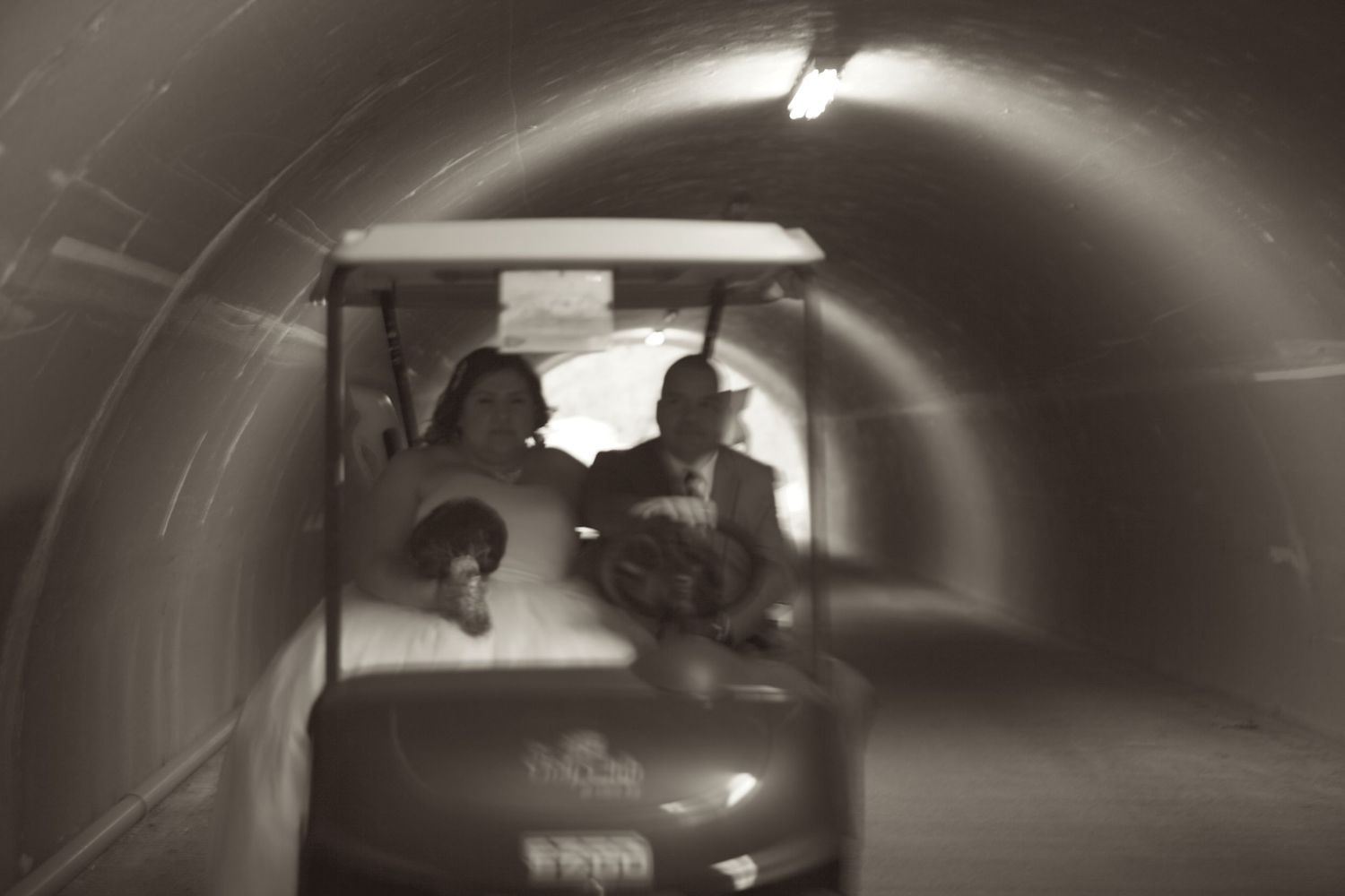 People riding a golf cart through a dimly lit tunnel, captured in a sepia-toned, motion-blurred photograph.
