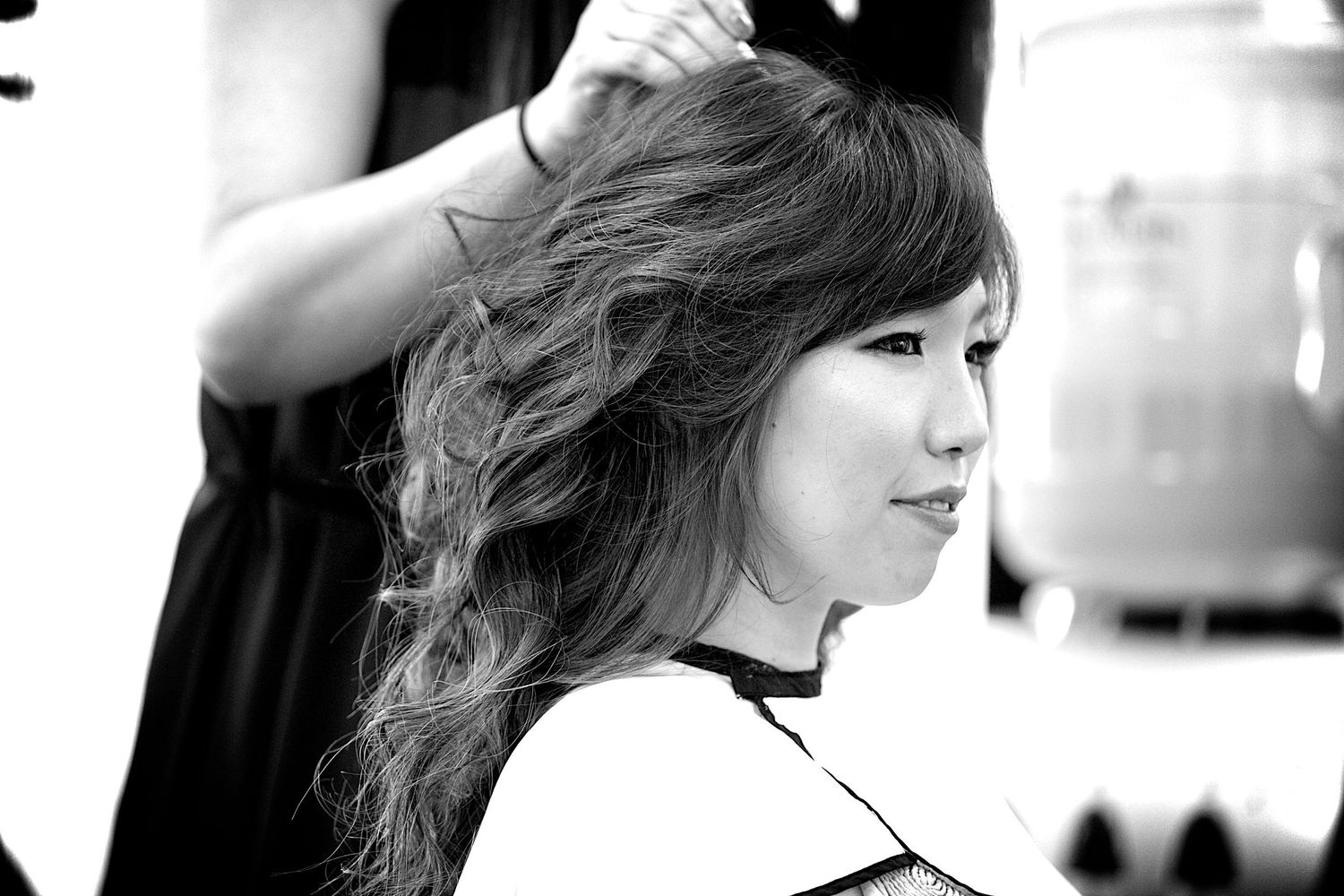 Black and white photo of a woman getting her long wavy hair styled at a salon.