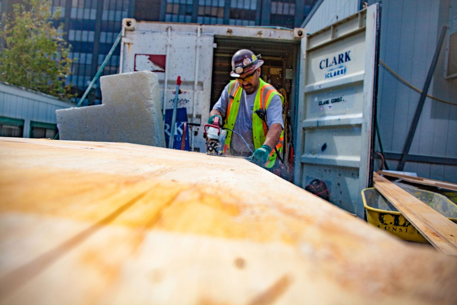 Construction worker unloading lumber from a Clark container truck at an active building site.