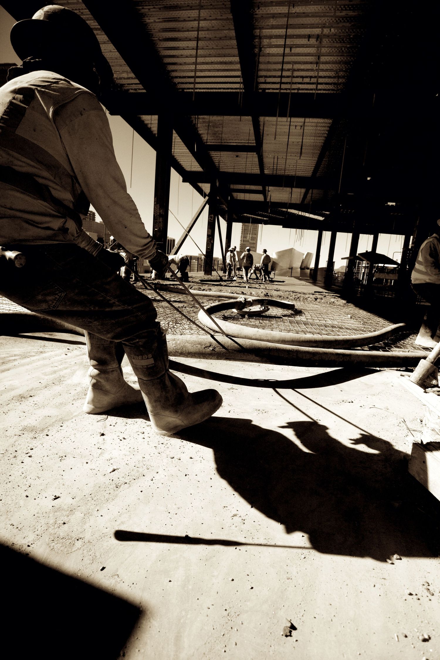Low angle sepia photo of a construction worker pulling cables on a job site floor.
