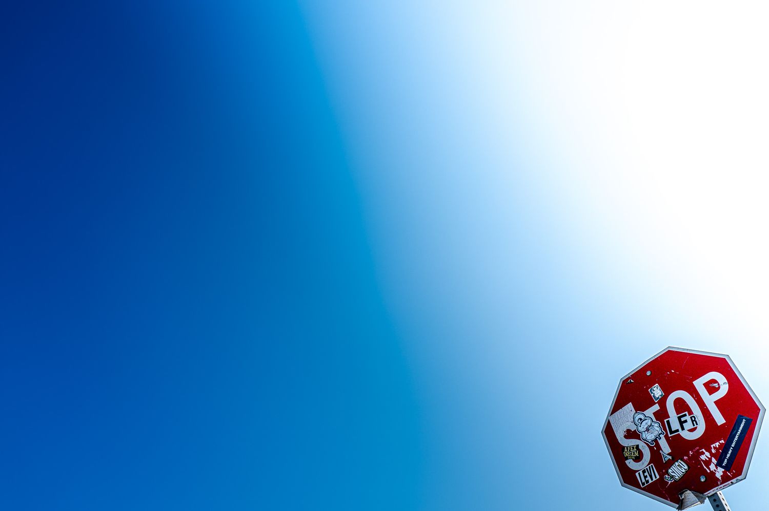 A red stop sign against a vivid blue sky with bright sunlight, photographed from a low angle perspective.