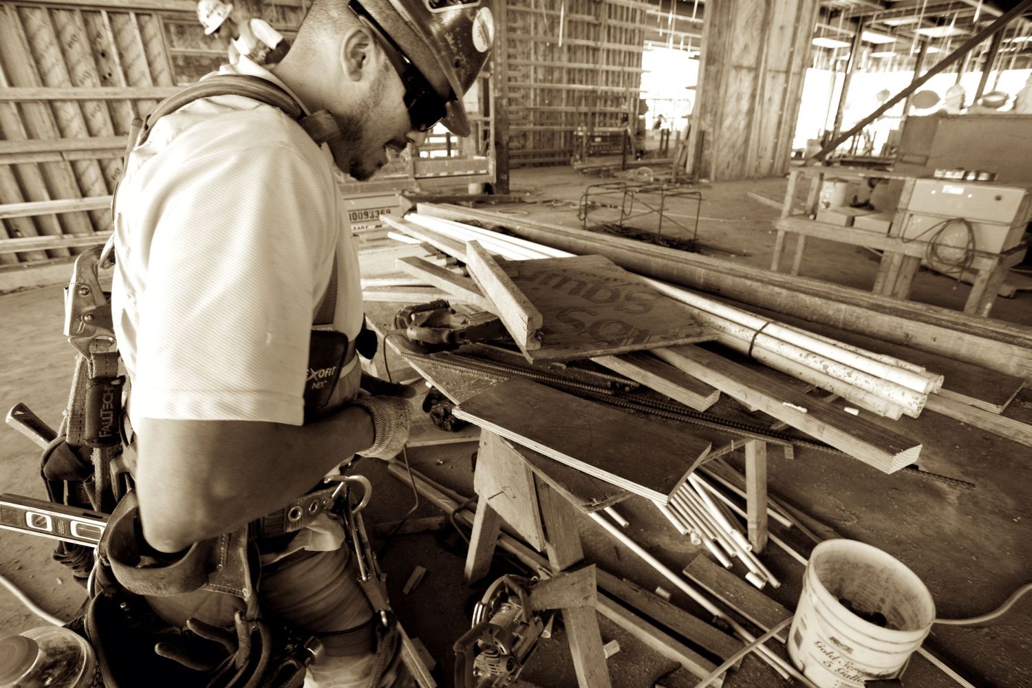 Construction worker in hard hat examining lumber and building materials at a job site.