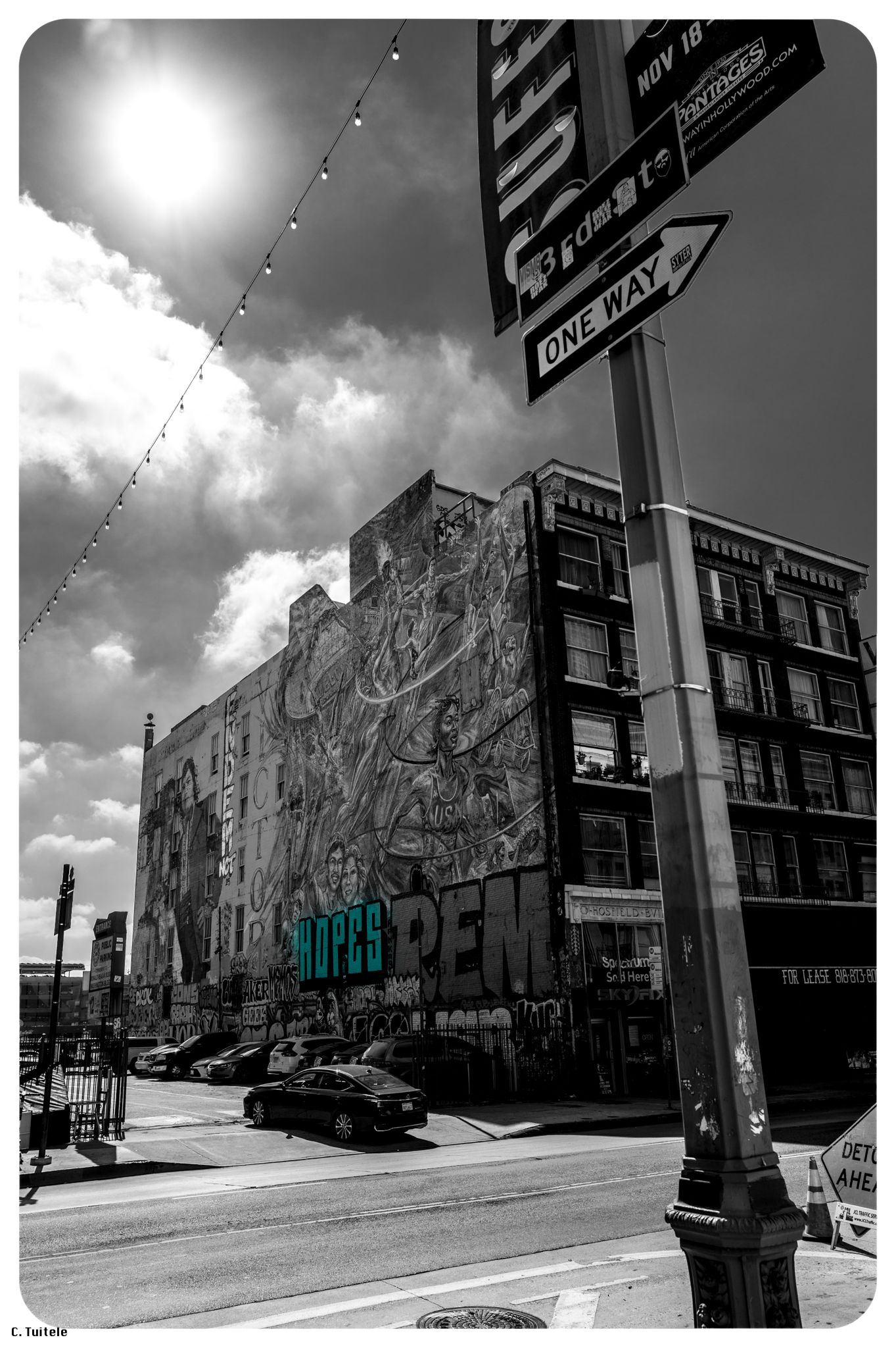 Black and white urban street corner with large graffiti mural and one way sign.