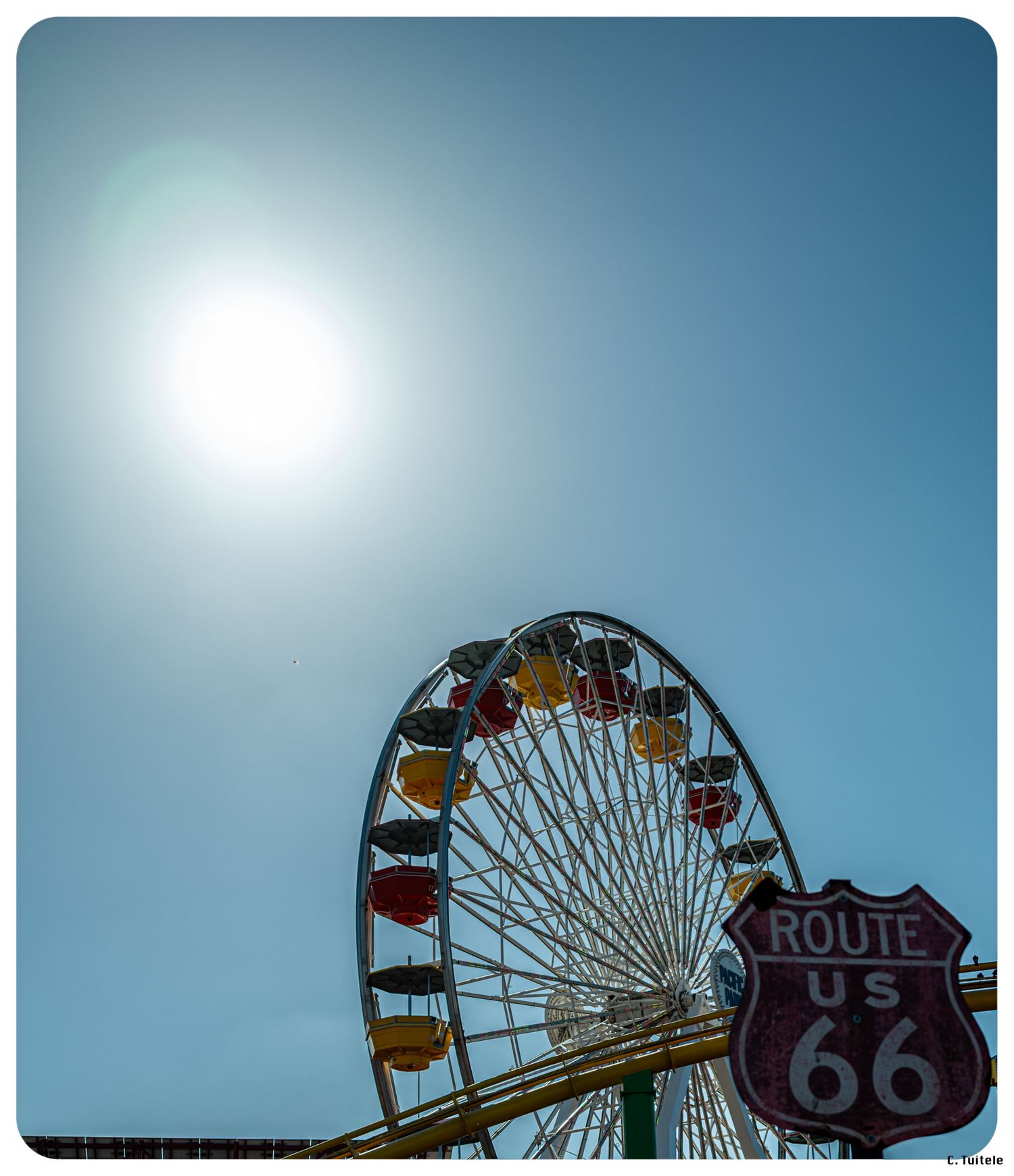 Ferris wheel and Route 66 sign against a bright blue sky with sun.