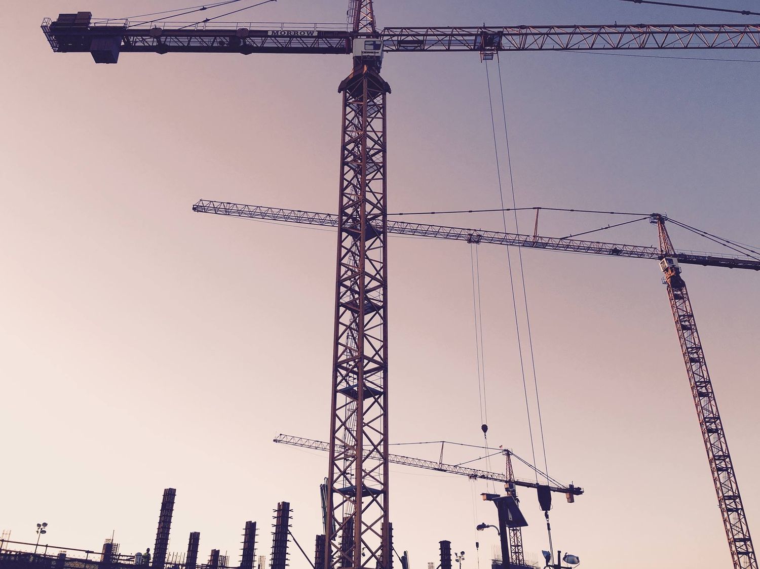 Construction worker in medical jersey and hard hat surveying a building site with scaffolding.