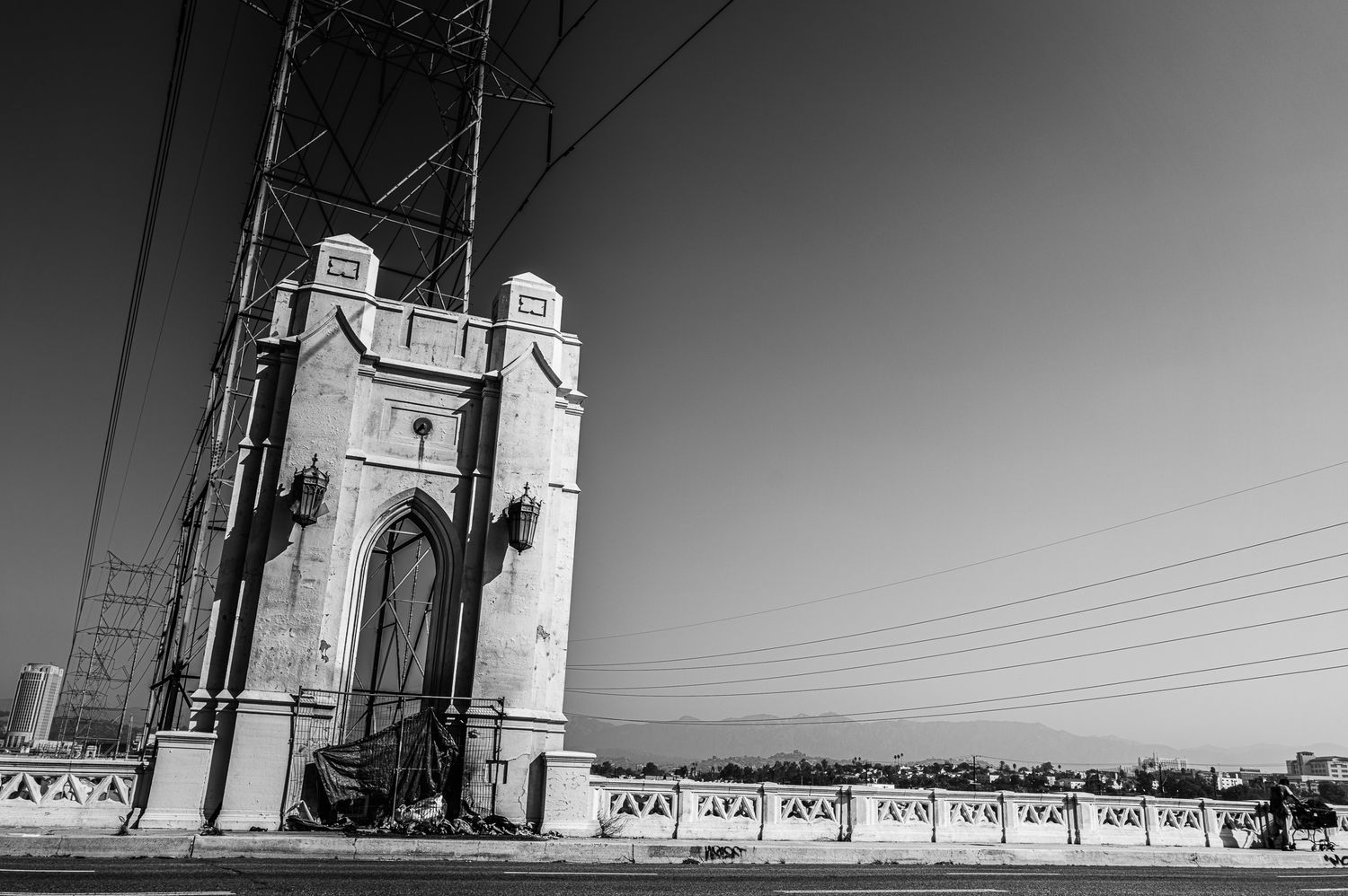 Black and white photo of a historic stone bridge tower with power lines against a clear sky.