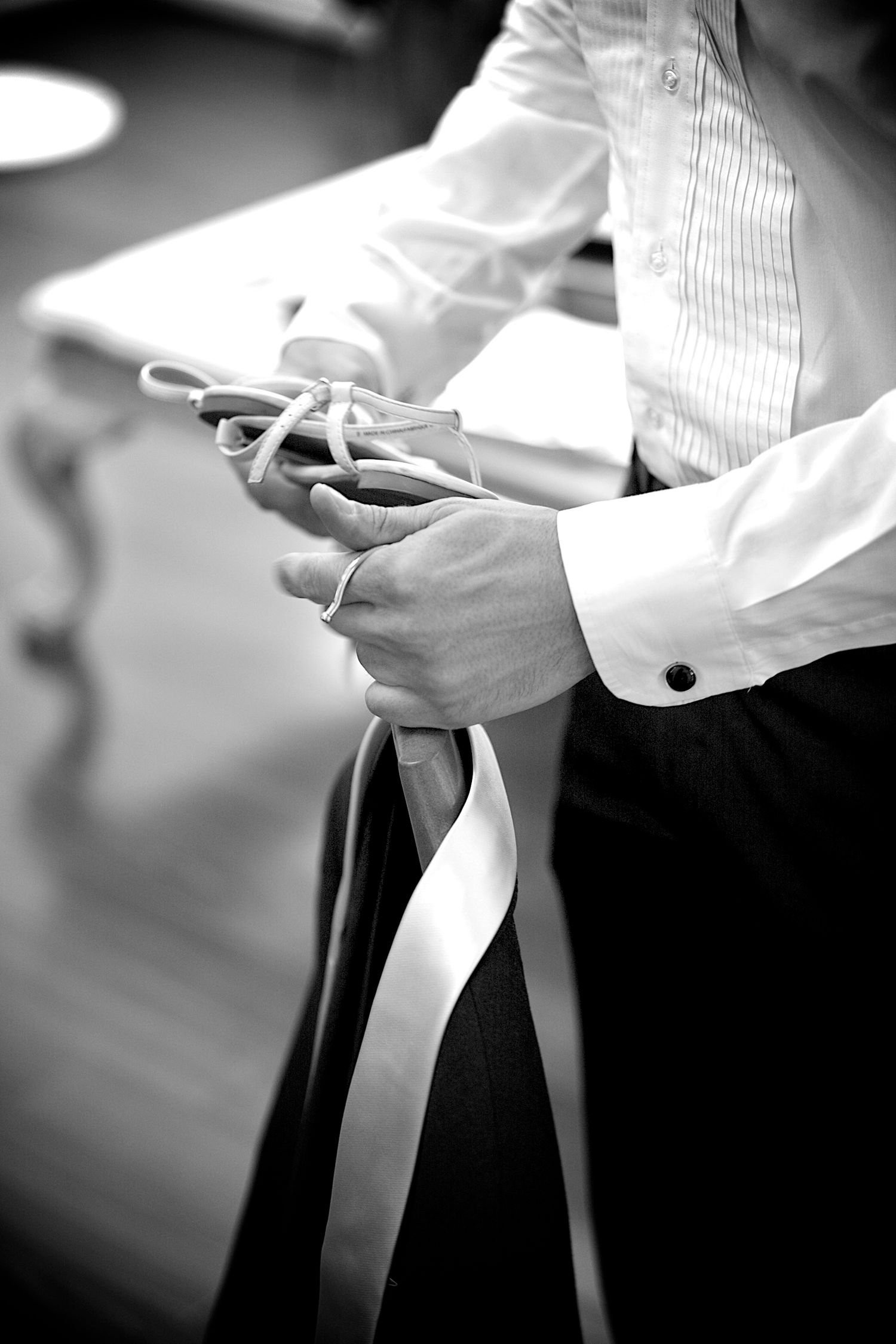 Black and white photo of a groom holding wedding ribbon and rope during ceremony preparations.