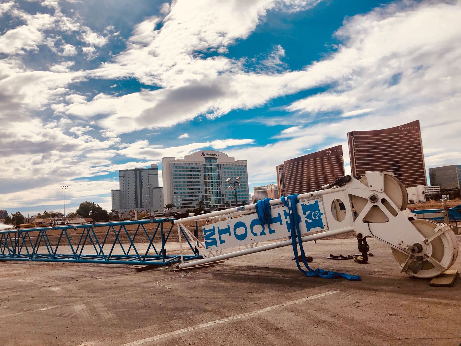 Construction crane lying on ground at Las Vegas Strip with casino hotels and cloudy blue sky in background.