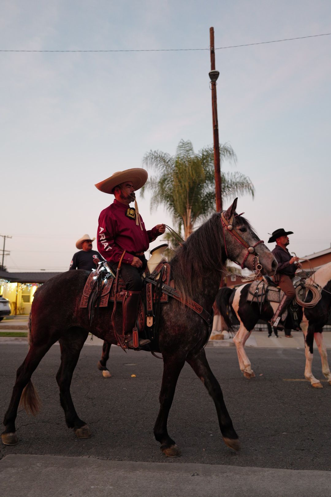 A charro rider in traditional Mexican attire on horseback during a street parade at dusk.