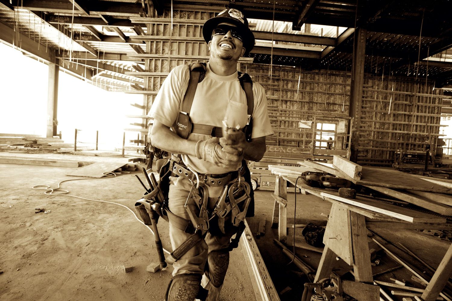 Smiling construction worker in hard hat and tool belt standing in an unfinished building site.