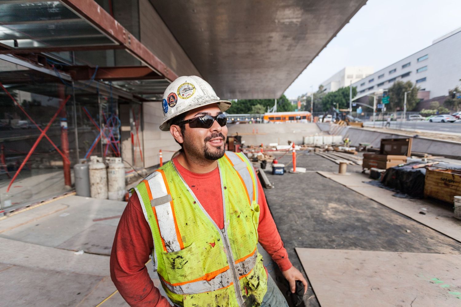 Smiling construction worker in yellow safety vest and hard hat at an urban job site.