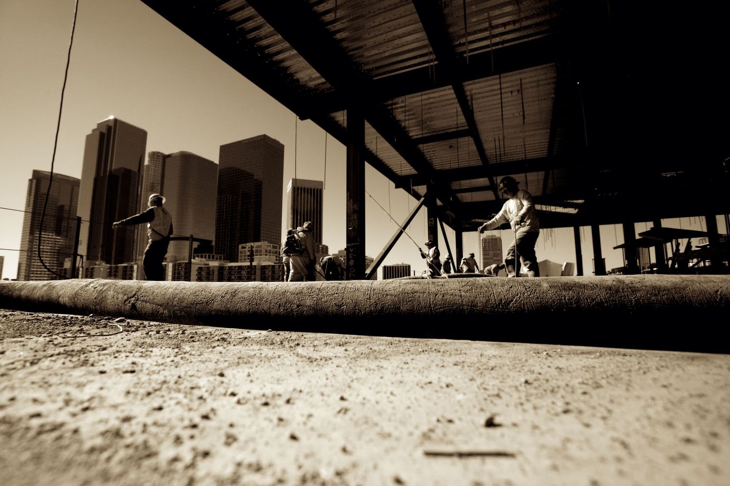 Sepia toned wide angle photo of workers rolling out material at a construction site.