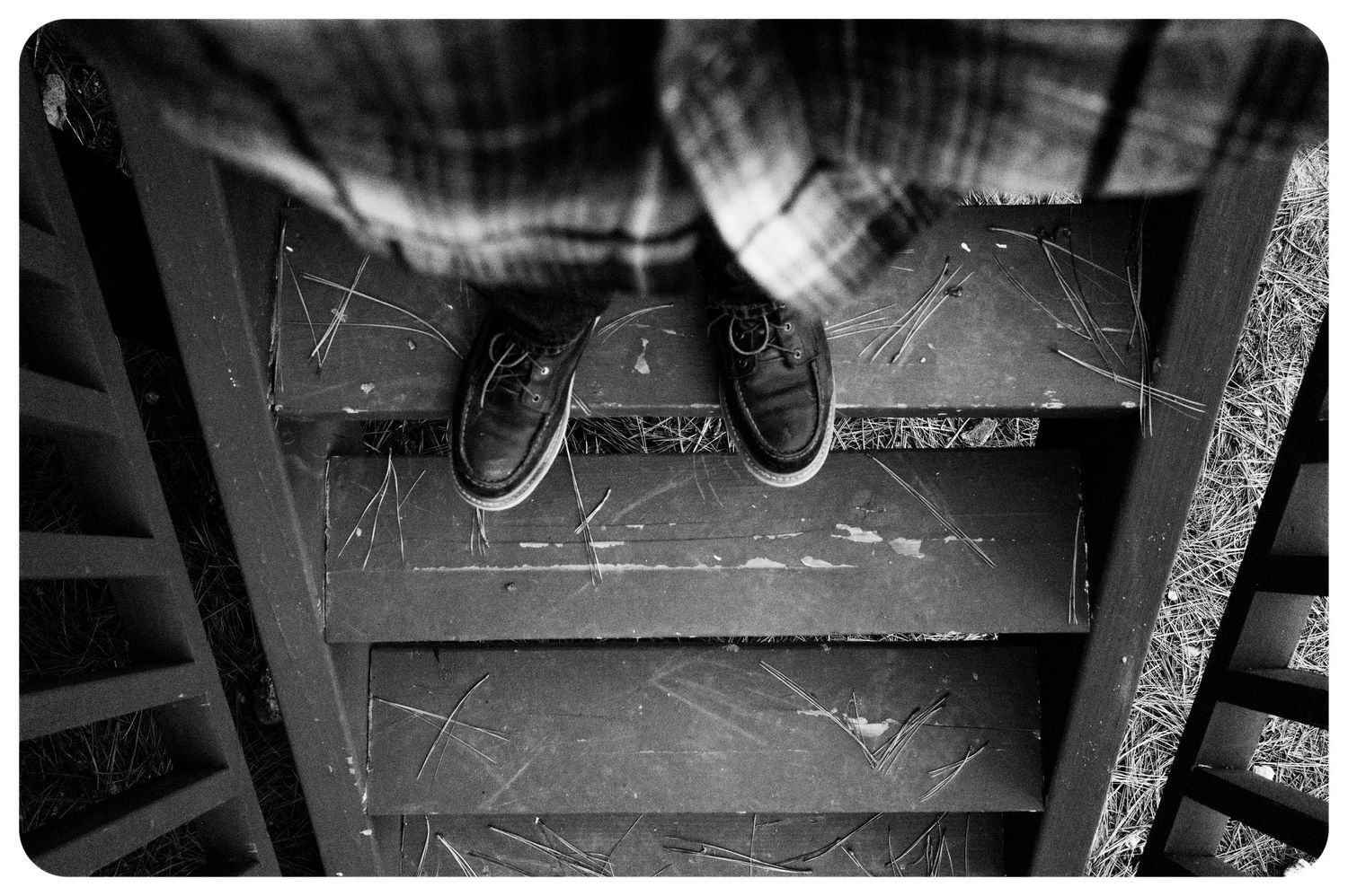 Black and white overhead view of worn shoes standing on scratched wooden stair steps.