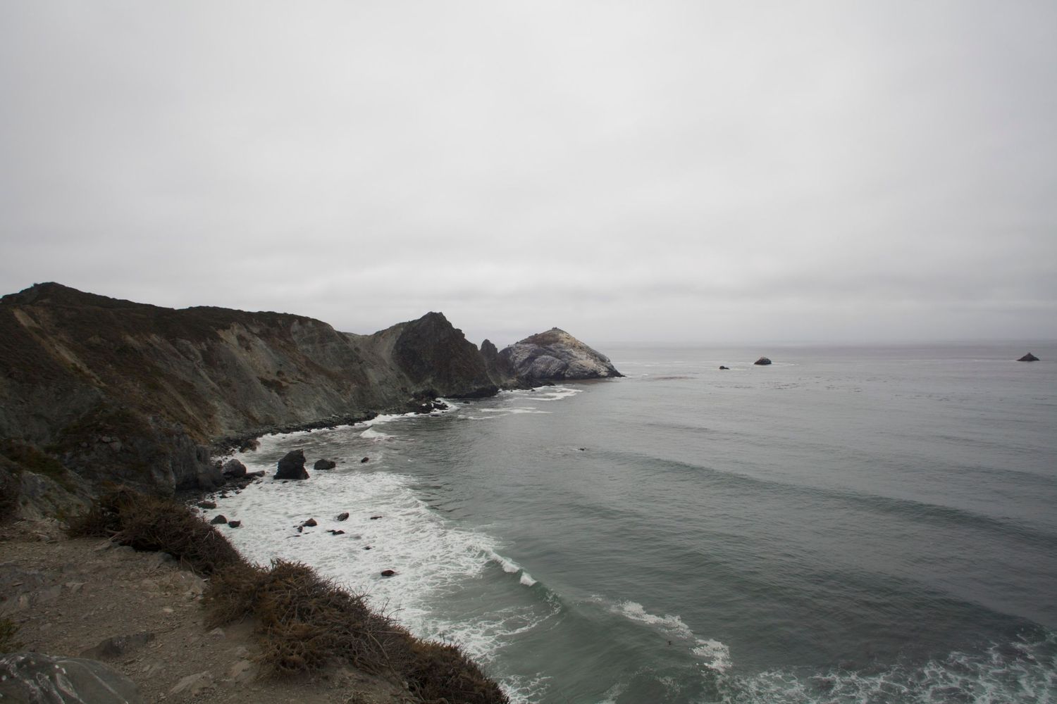 Dramatic coastal cliffs overlooking the Pacific Ocean on a foggy overcast day along California's scenic Big Sur coastline.