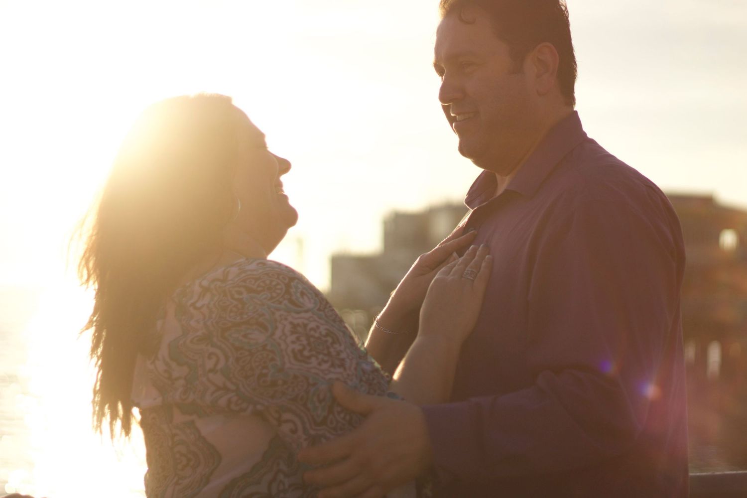 Romantic couple embracing at sunset with warm golden backlight creating a beautiful silhouette effect.