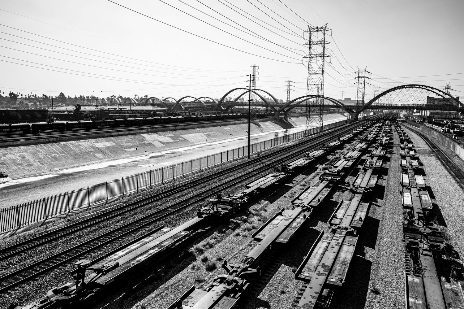 Black and white aerial view of parallel train tracks with arched bridges and electrical towers in an urban rail yard.