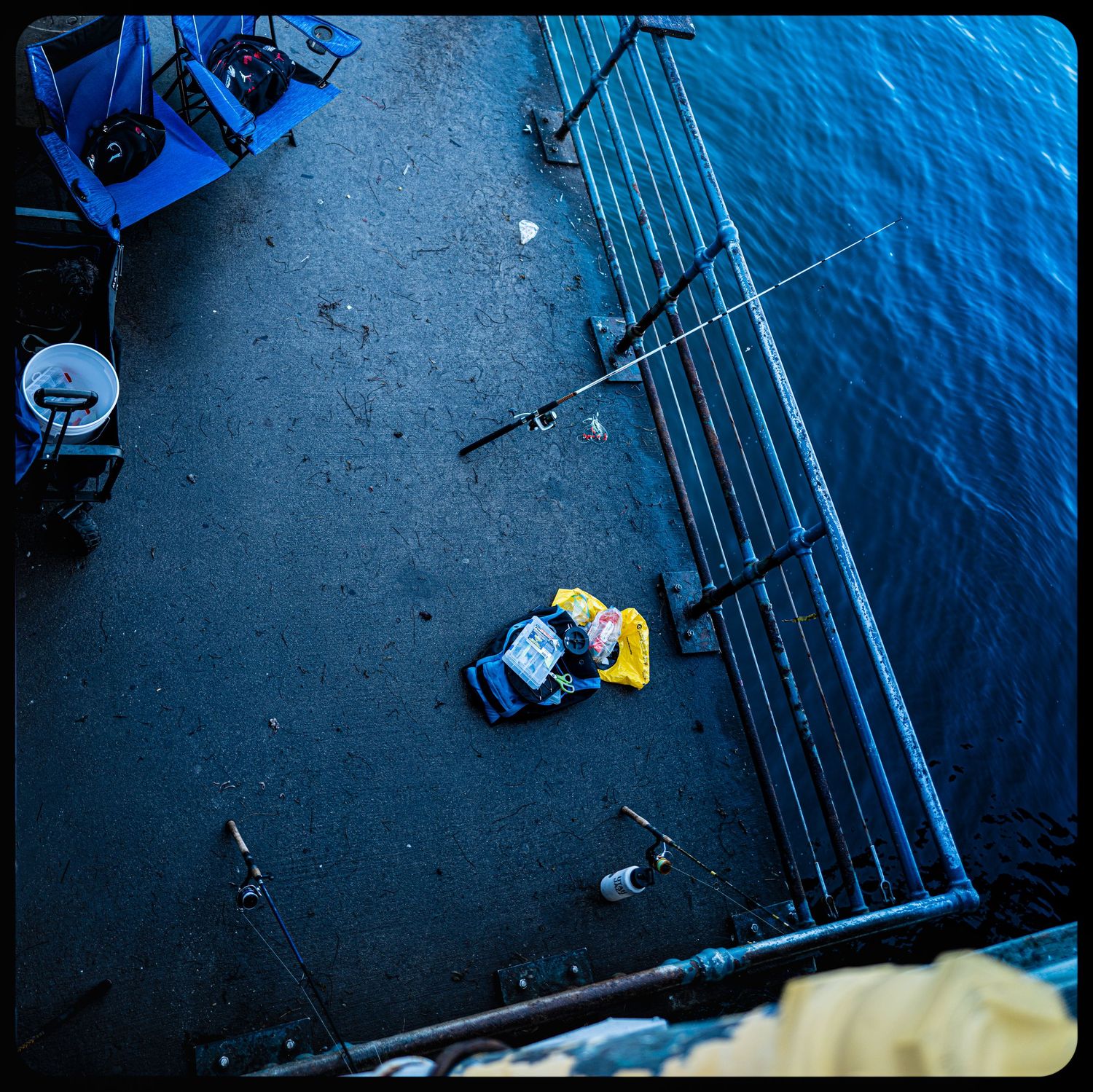Aerial view of worker in yellow jacket on dark wet dock beside blue ocean.