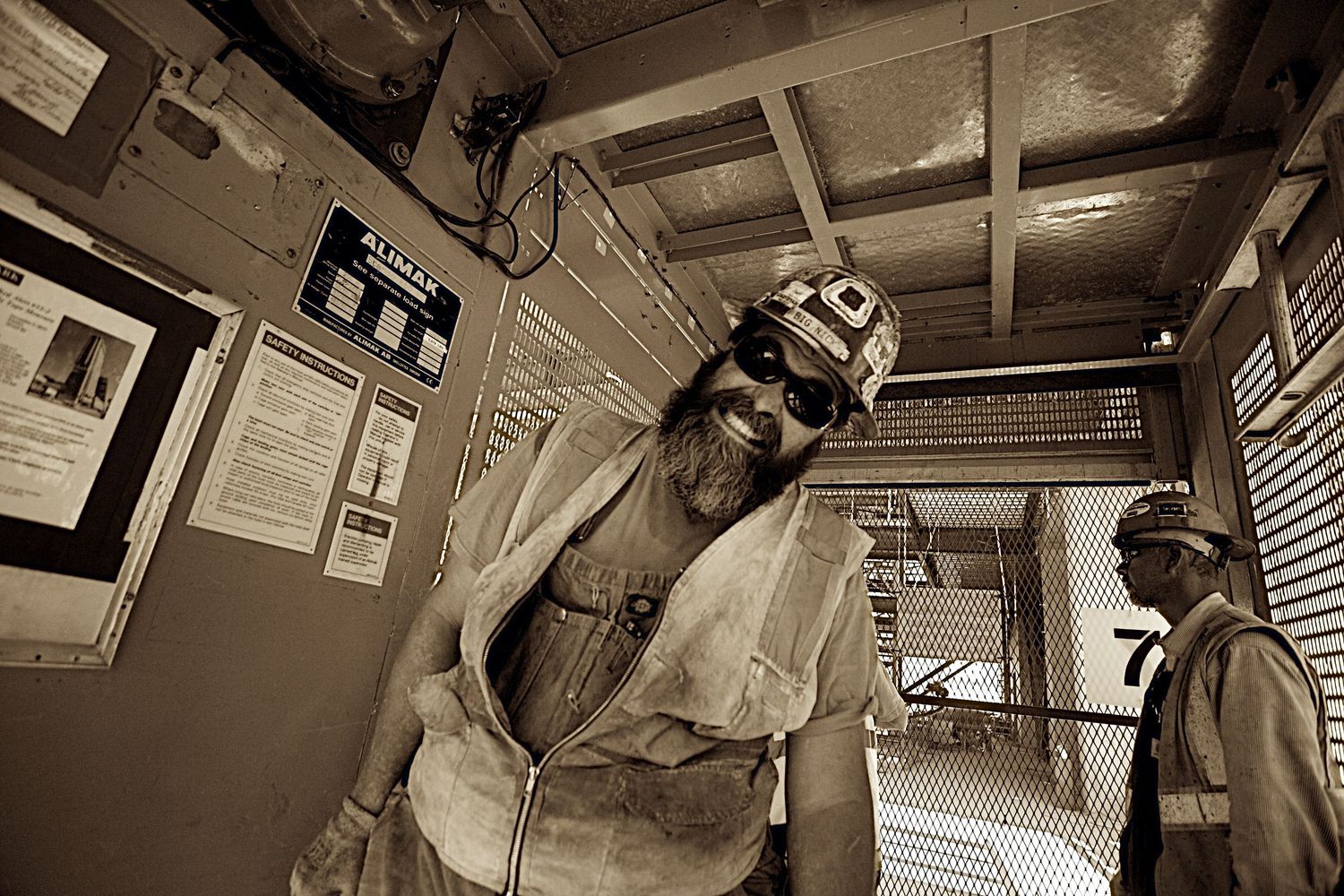 Sepia toned photo of two construction workers in hard hats inside an industrial building.