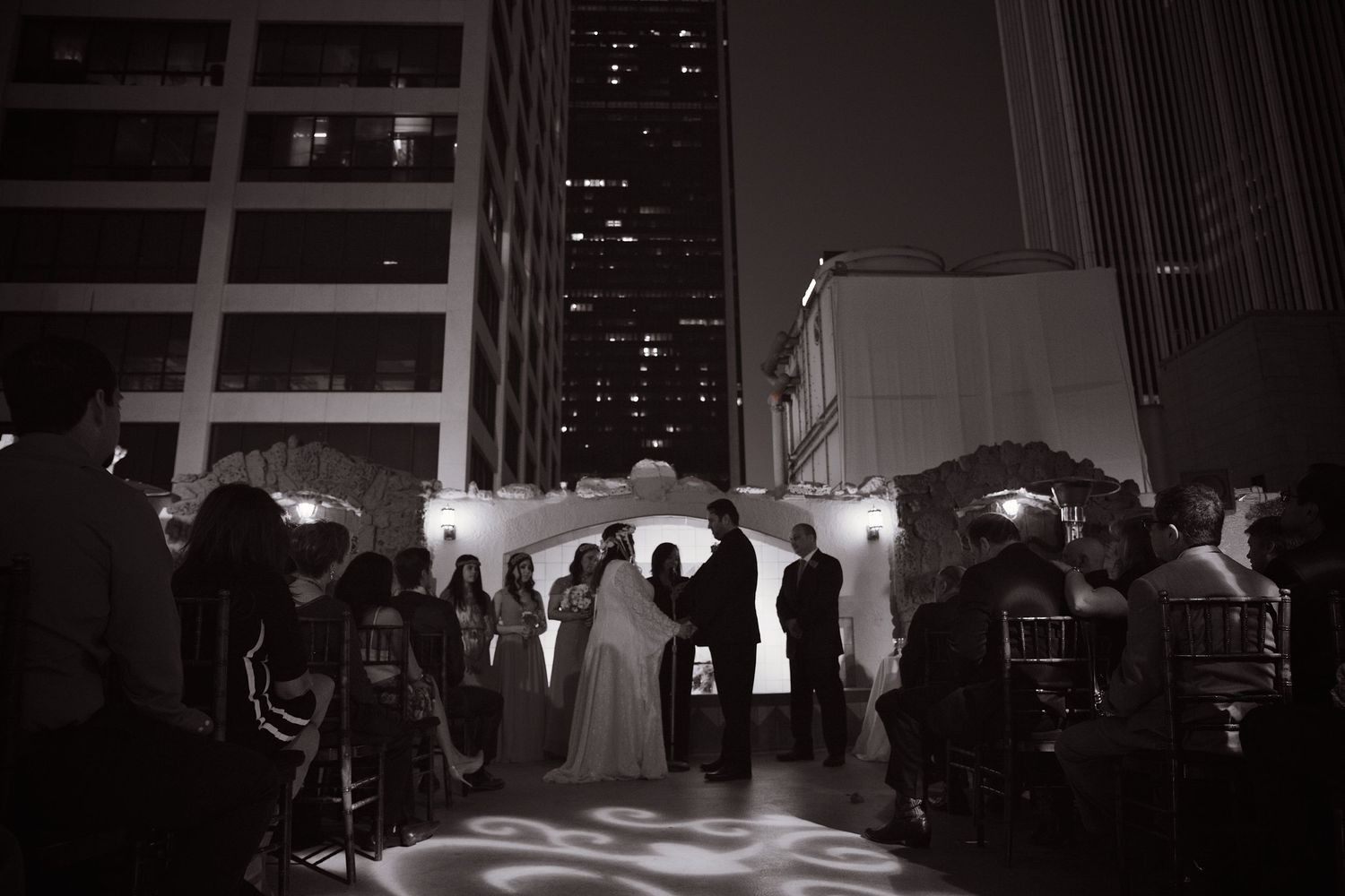 Black and white photo of an outdoor rooftop wedding ceremony at night in the city.
