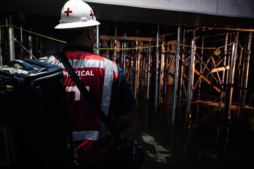 Medical personnel in red cross vest navigating dark scaffolding at an underground construction site.