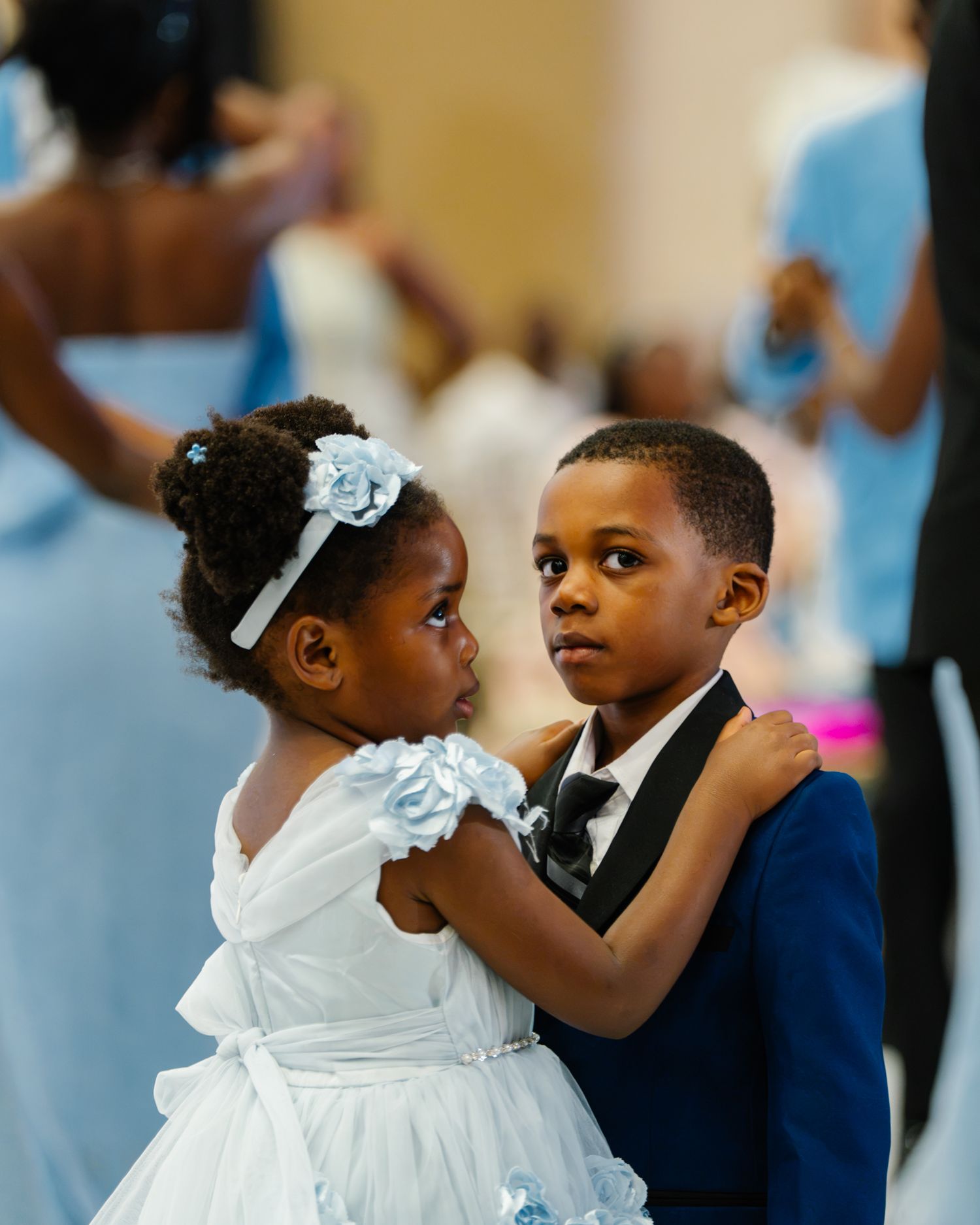 A young girl in a white dress dances with a boy in a navy suit at a wedding reception.