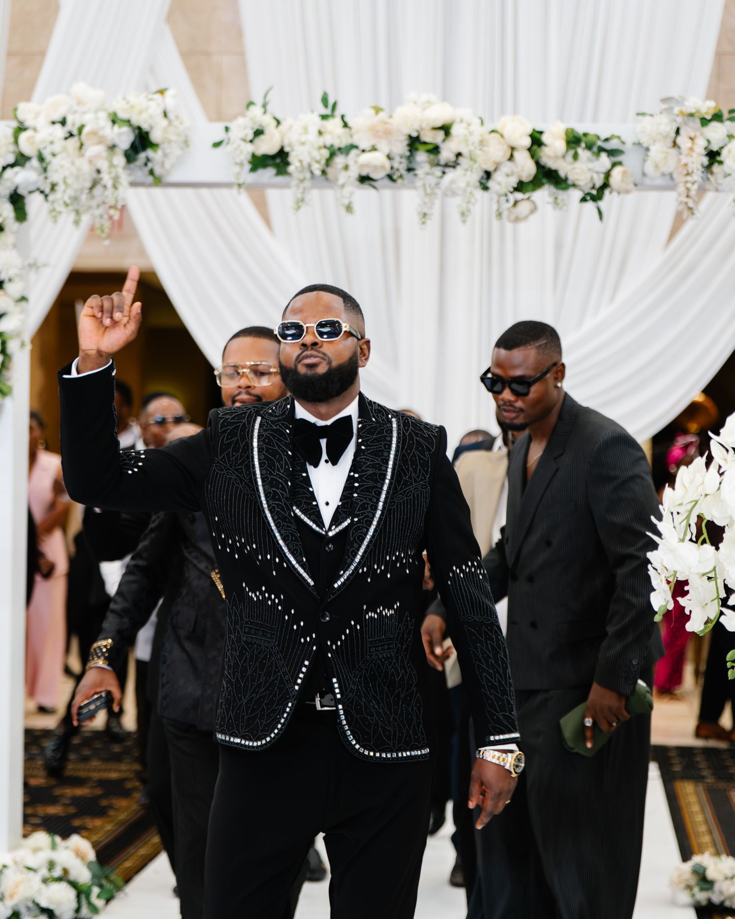 A groom in a black sequined tuxedo walks down the aisle at a formal wedding ceremony.