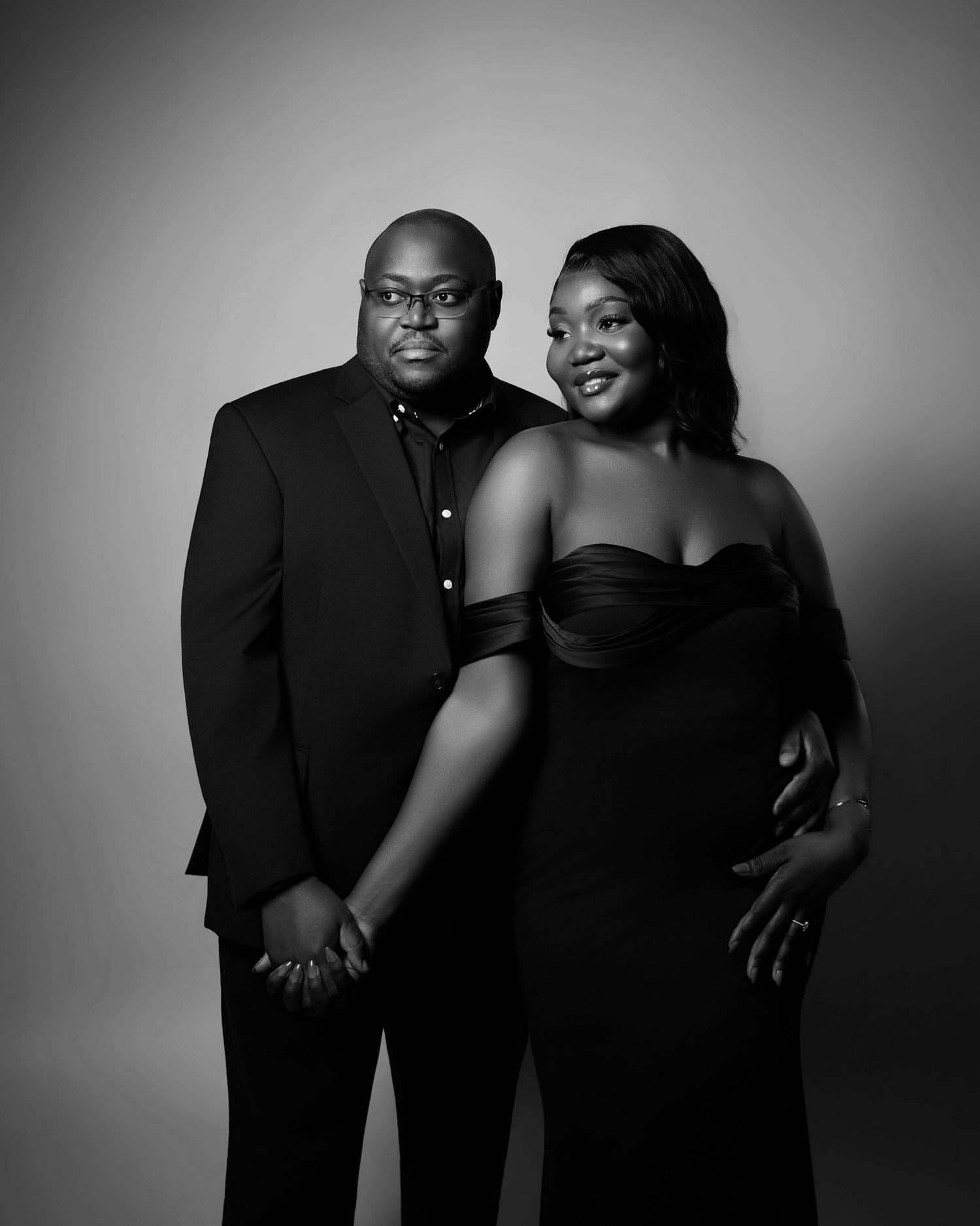 Elegant black and white portrait of a couple dressed in formal black attire in a studio setting.