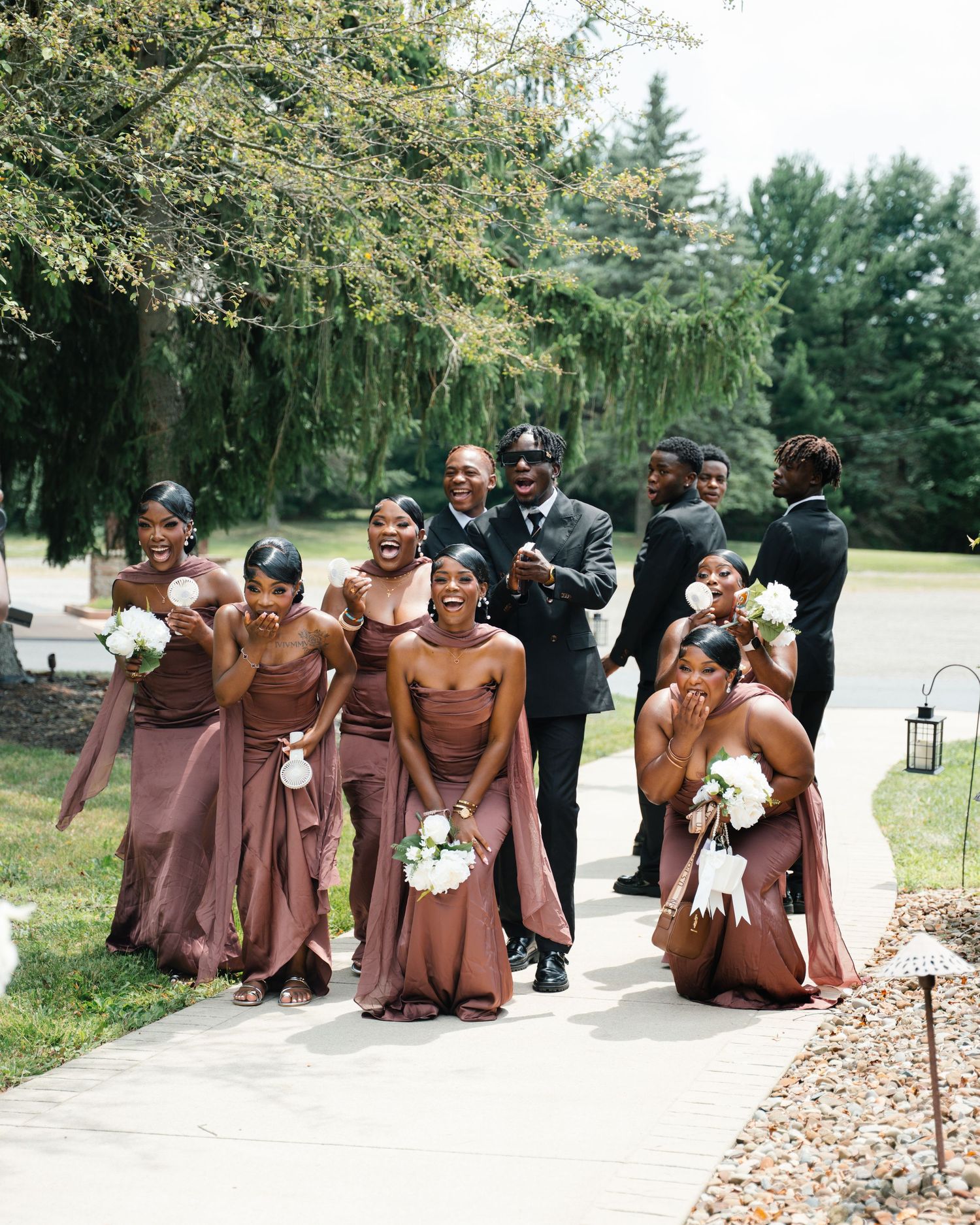 Bridesmaids in mauve gowns reacting emotionally during an outdoor wedding ceremony procession.