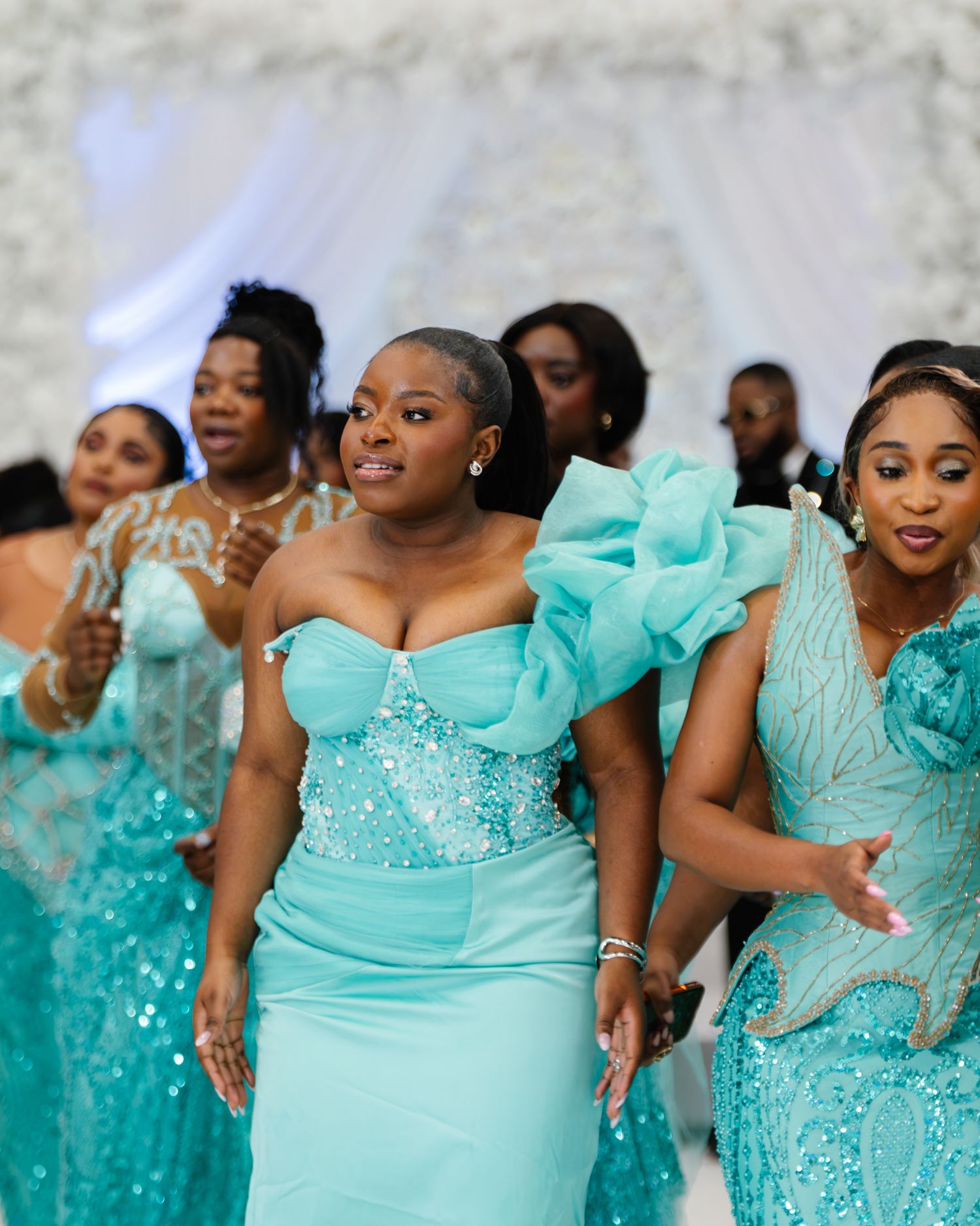 Bridesmaids in elegant turquoise gowns walk during a wedding ceremony procession.