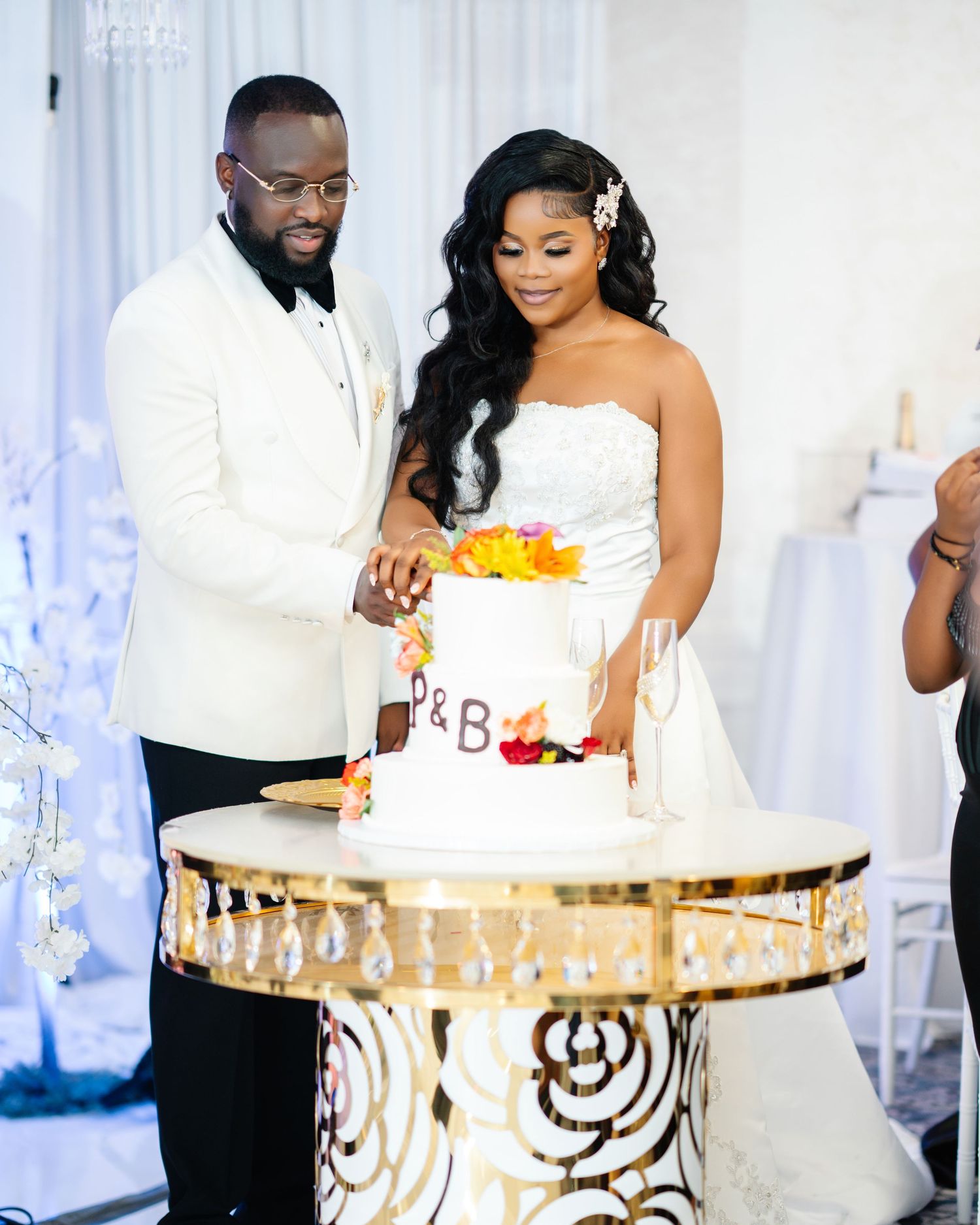 Bride and groom cutting their elegant two-tier wedding cake on a gold decorative table at reception.