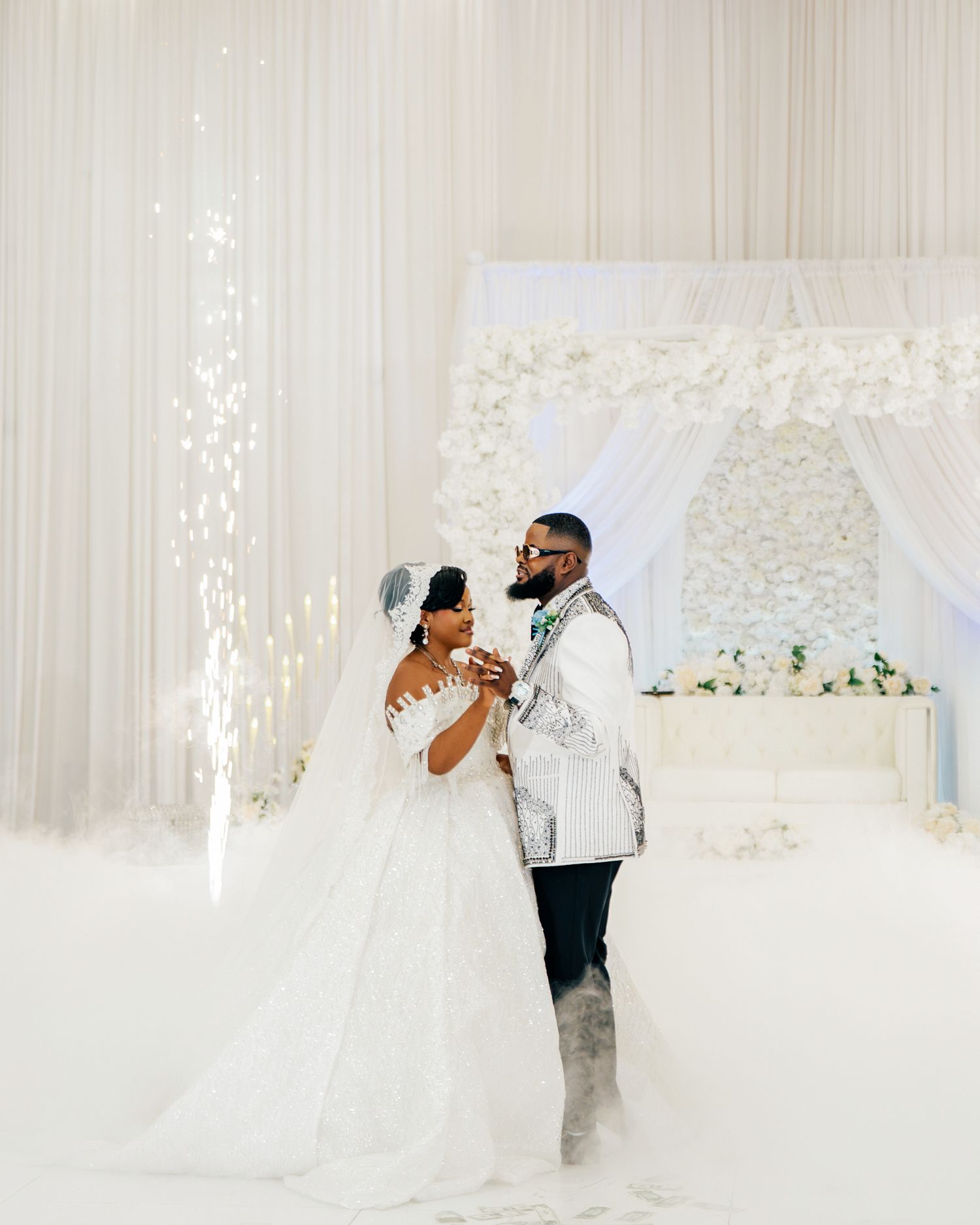 Newlyweds share first dance surrounded by sparkling lights and white floral arch at elegant wedding.