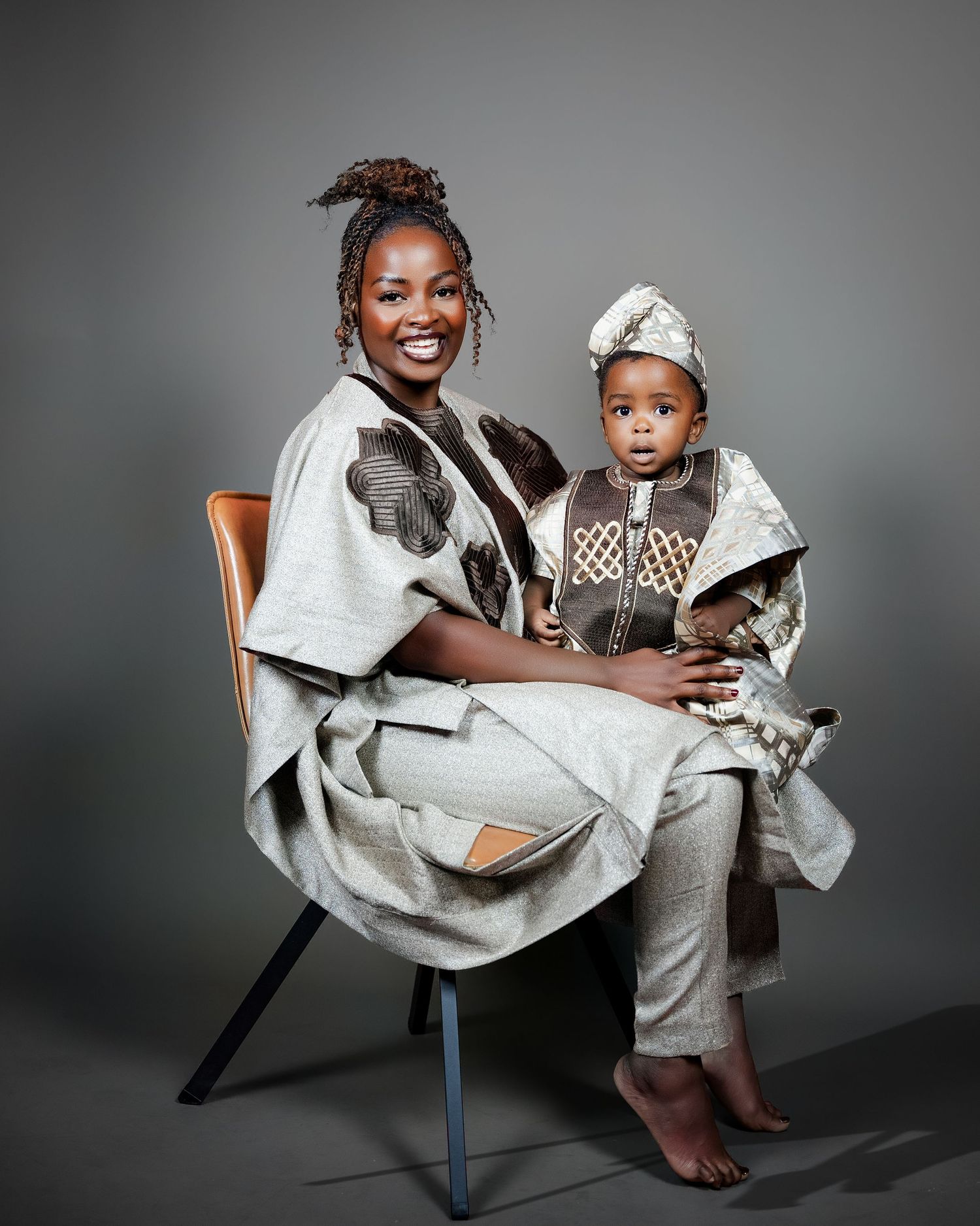A joyful mother and toddler wearing coordinating traditional African outfits in a professional studio portrait.