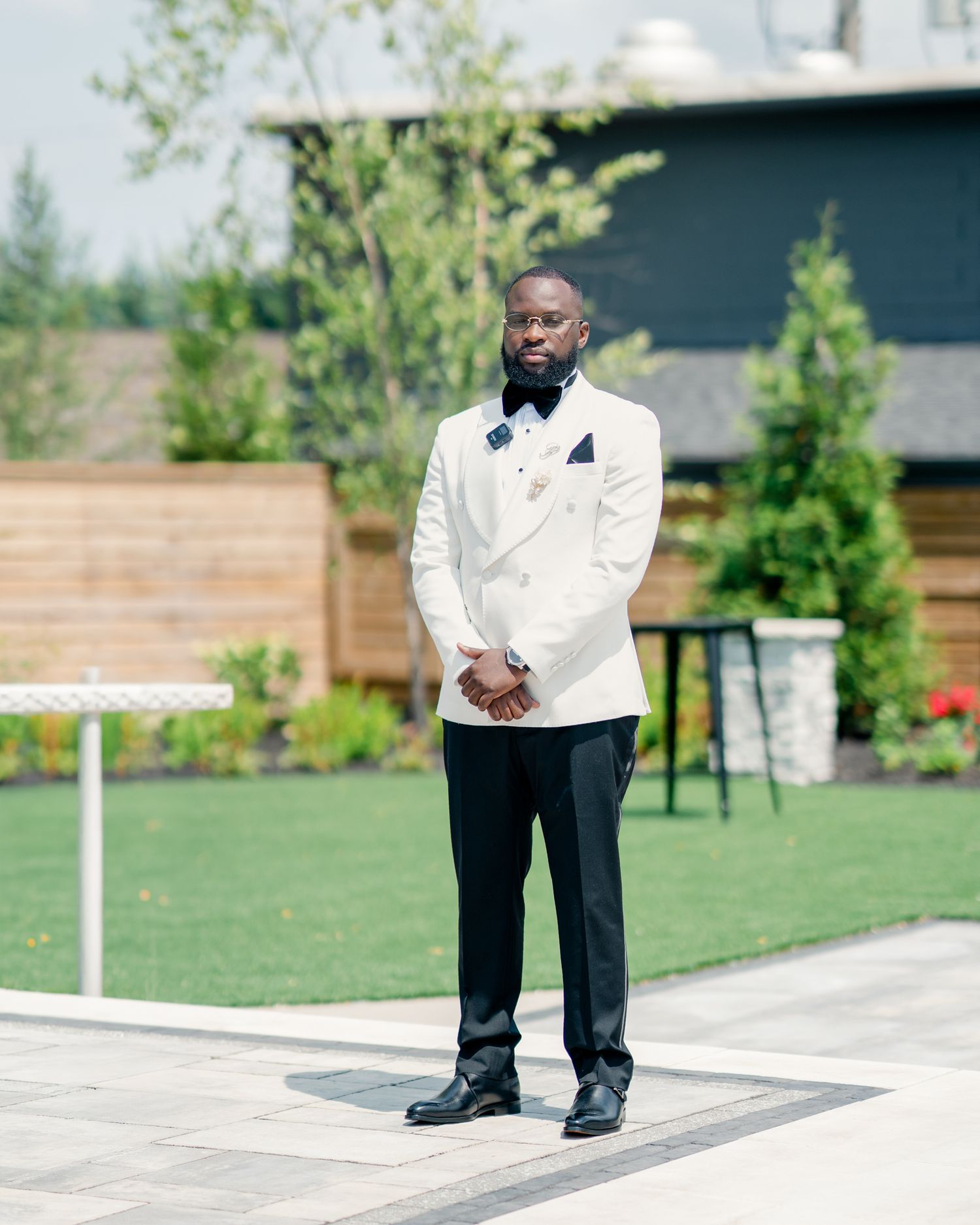 Dapper groom stands outdoors in white double-breasted tuxedo jacket with black bow tie.