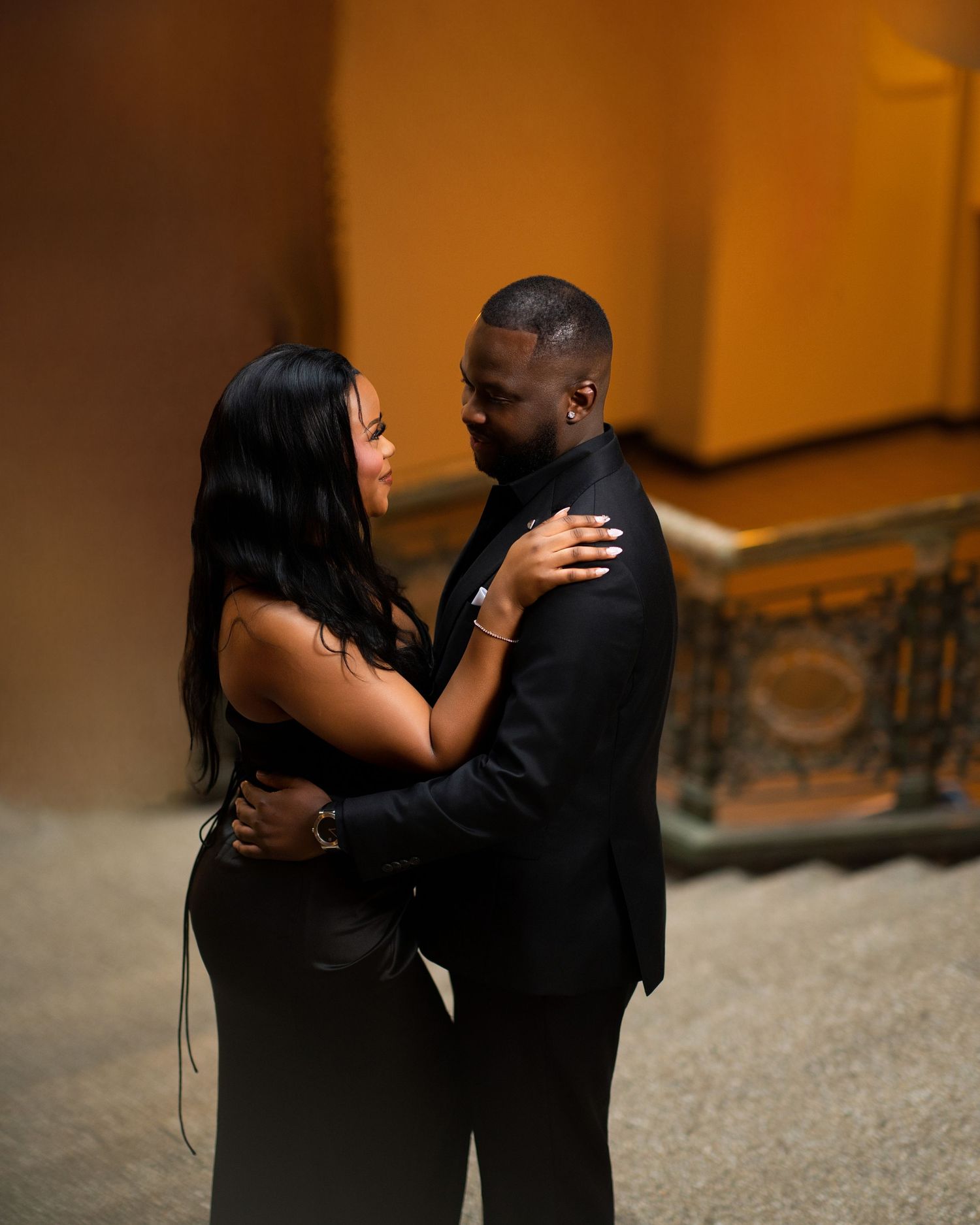 A couple in black formal wear sharing a romantic dance in a warmly lit venue.