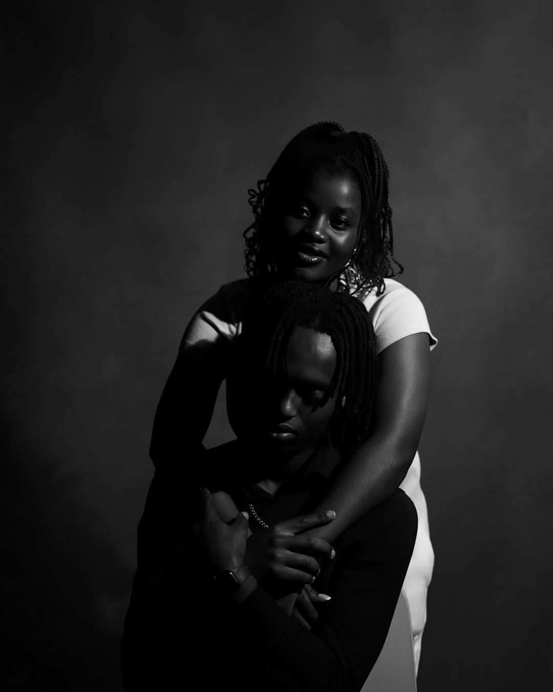 Black and white portrait of couple embracing in studio, woman hugging man from behind.
