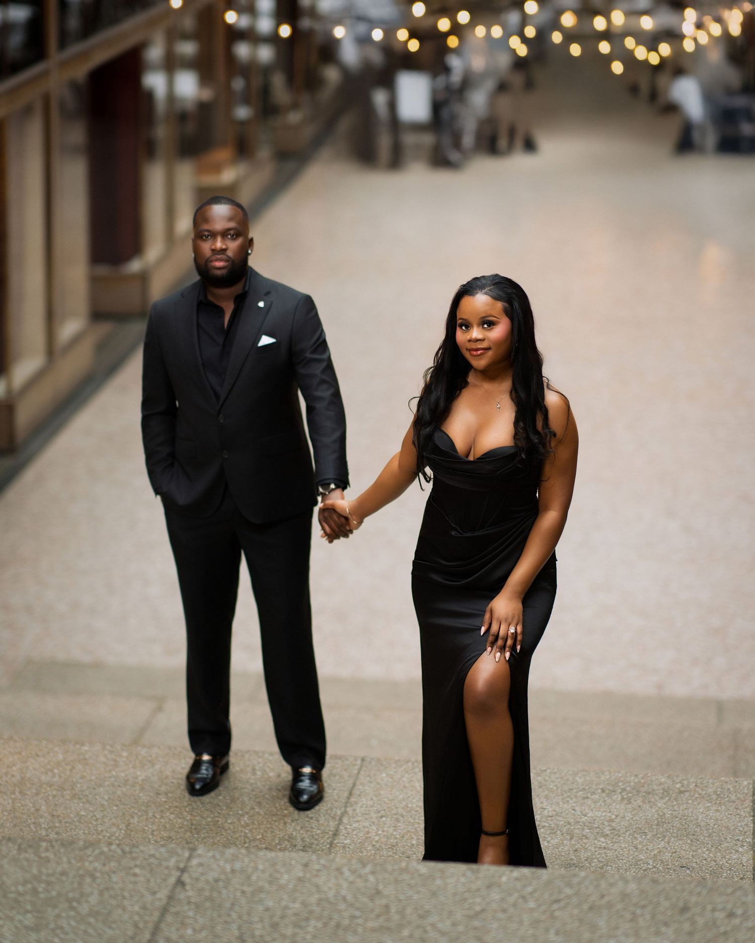 Stylish couple in matching black formal attire holding hands in elegant indoor venue.