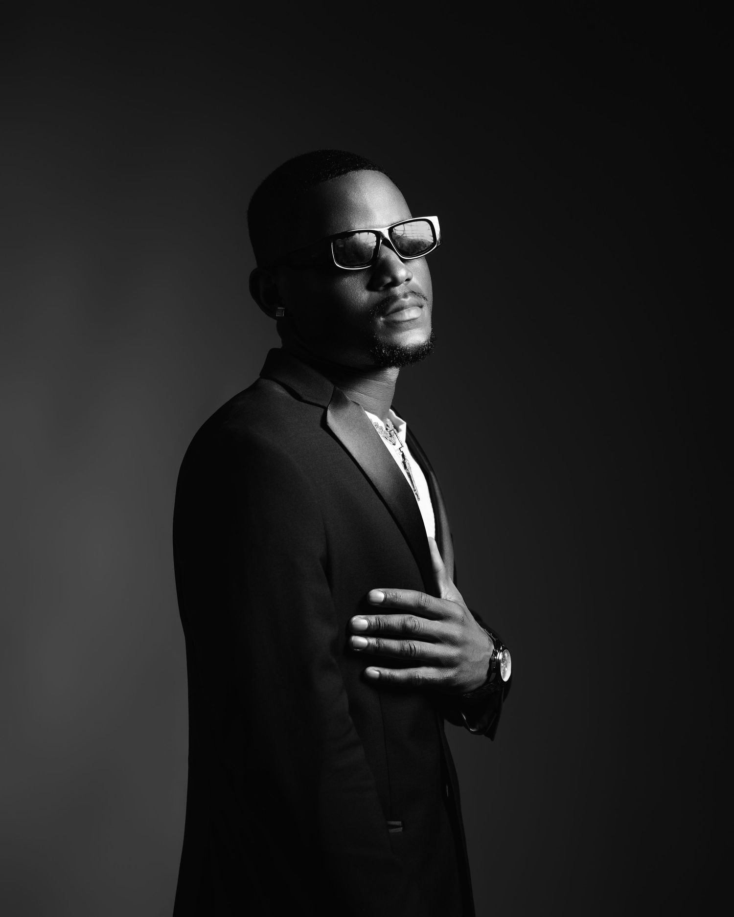 Black and white portrait of a stylish man in suit and sunglasses against dark background.
