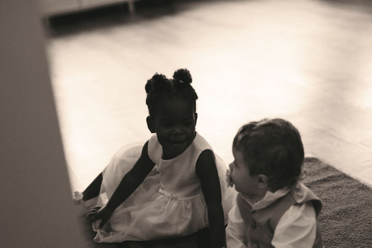 Two young children sitting together on the floor in black and white photo.